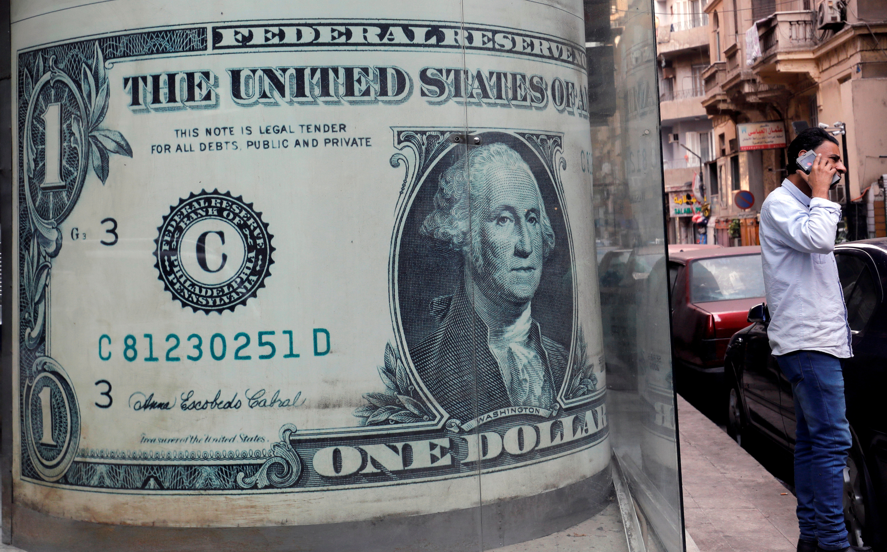 A man talks on his mobile phone in front of a currency exchange bureau advertisement showing images of the US dollar in Cairo, Egypt.