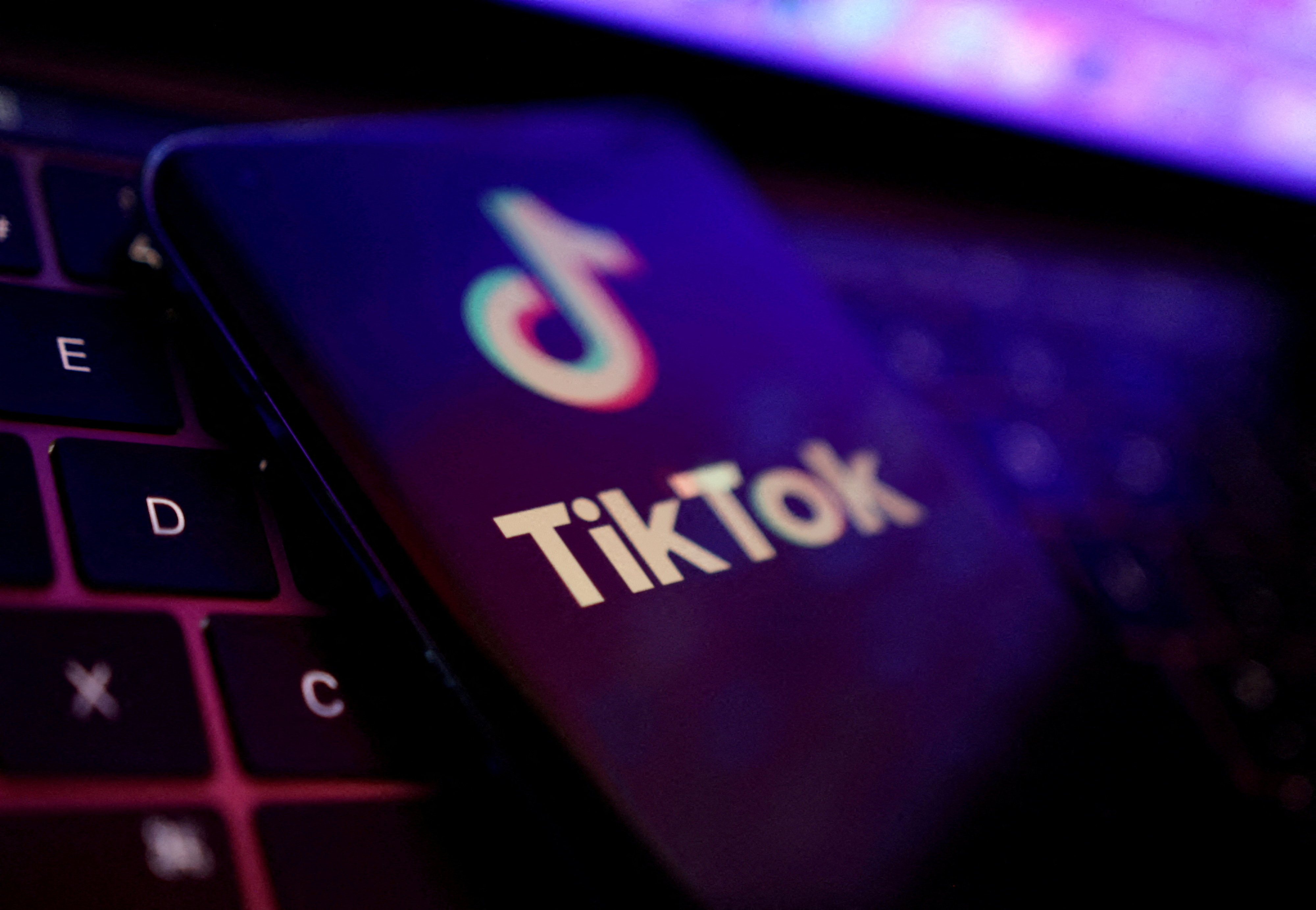 A picture showing a phone with the logo of the TikTok app on a laptop keyboard