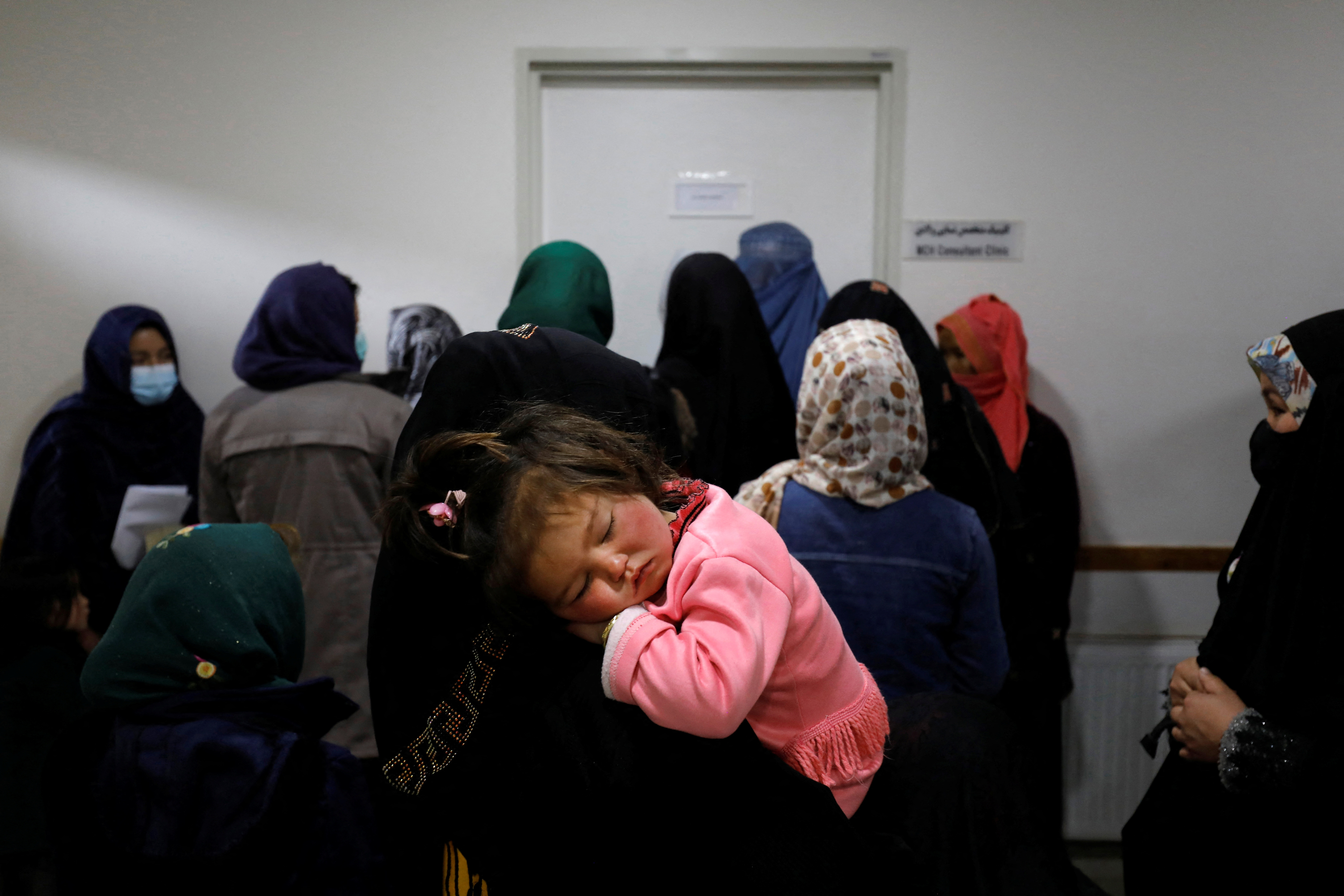 A mother holds her child as she rests in her arms, while women line up outside of a doctor's room, at a hospital in Bamiyan, Afghanistan