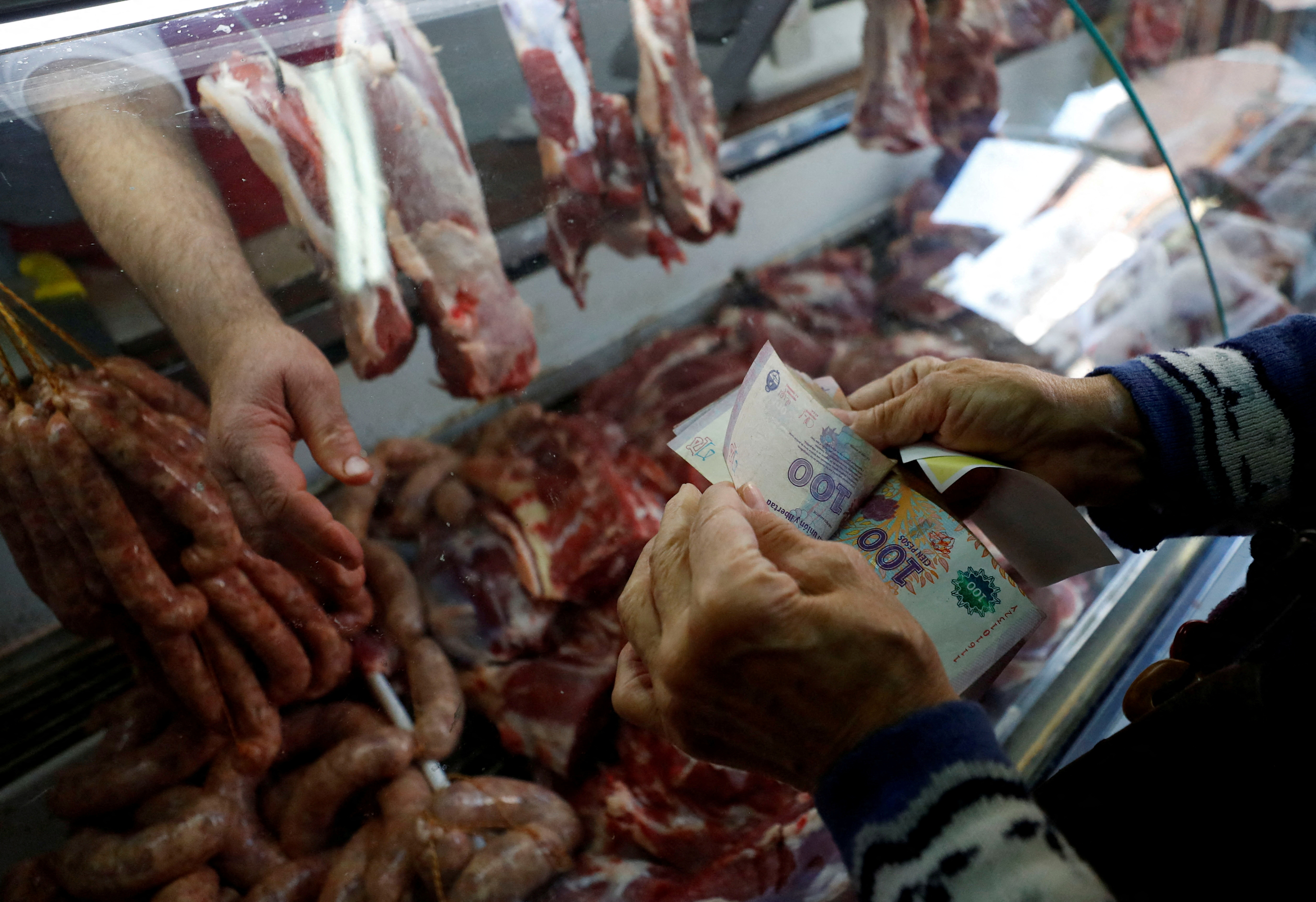 A man counts money in front of a butcher's counter