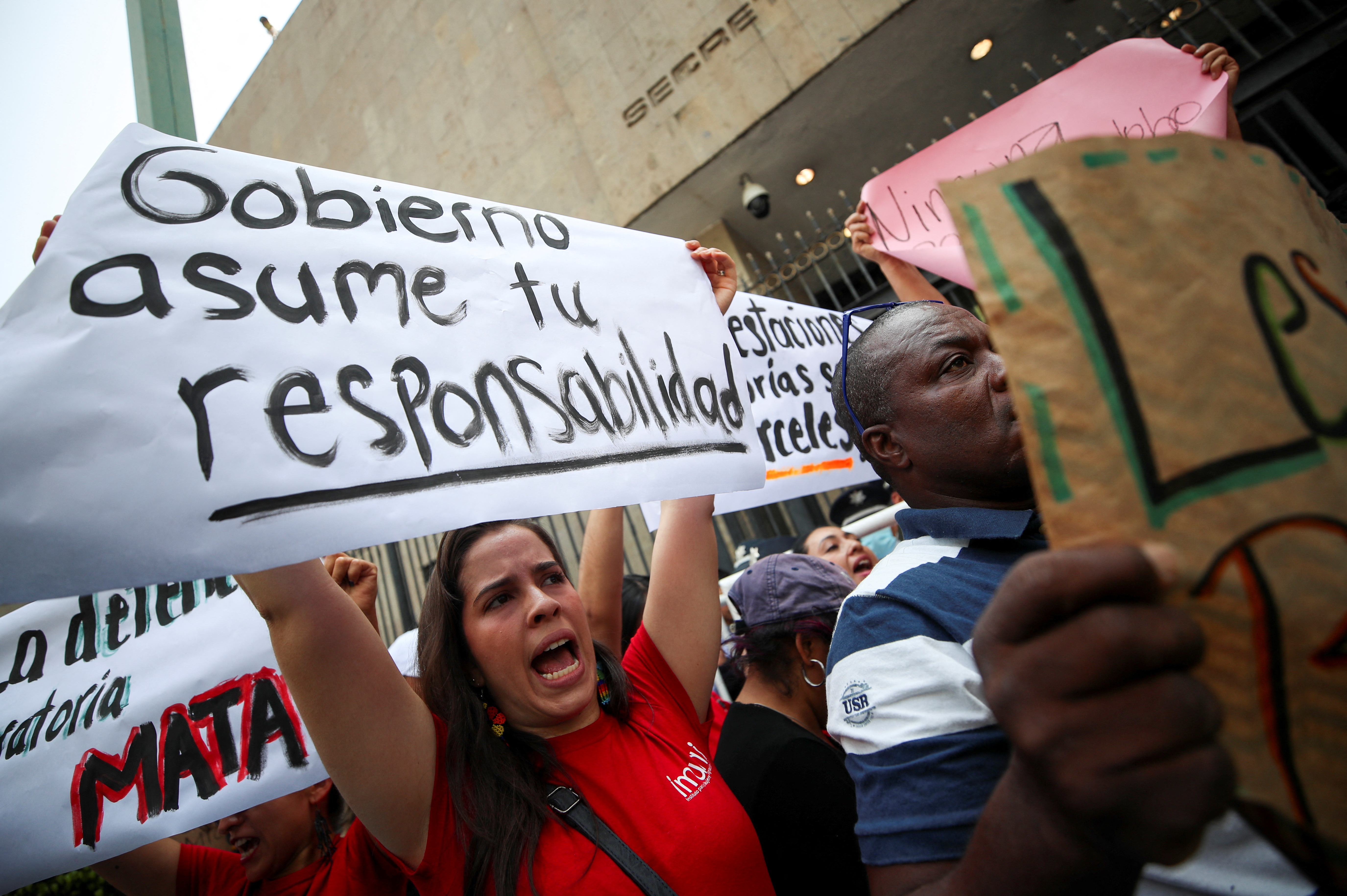 Demonstrators hold posters as they take part in a protest following the death of several migrants after a fire broke out at a migrant detention center late Monday