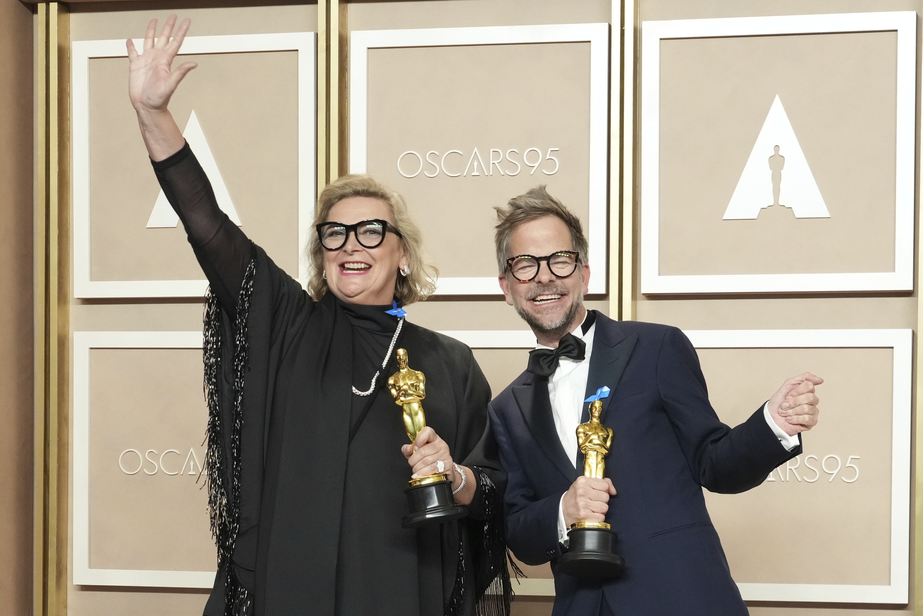 A woman waves her hand high, while a man leans over to pose