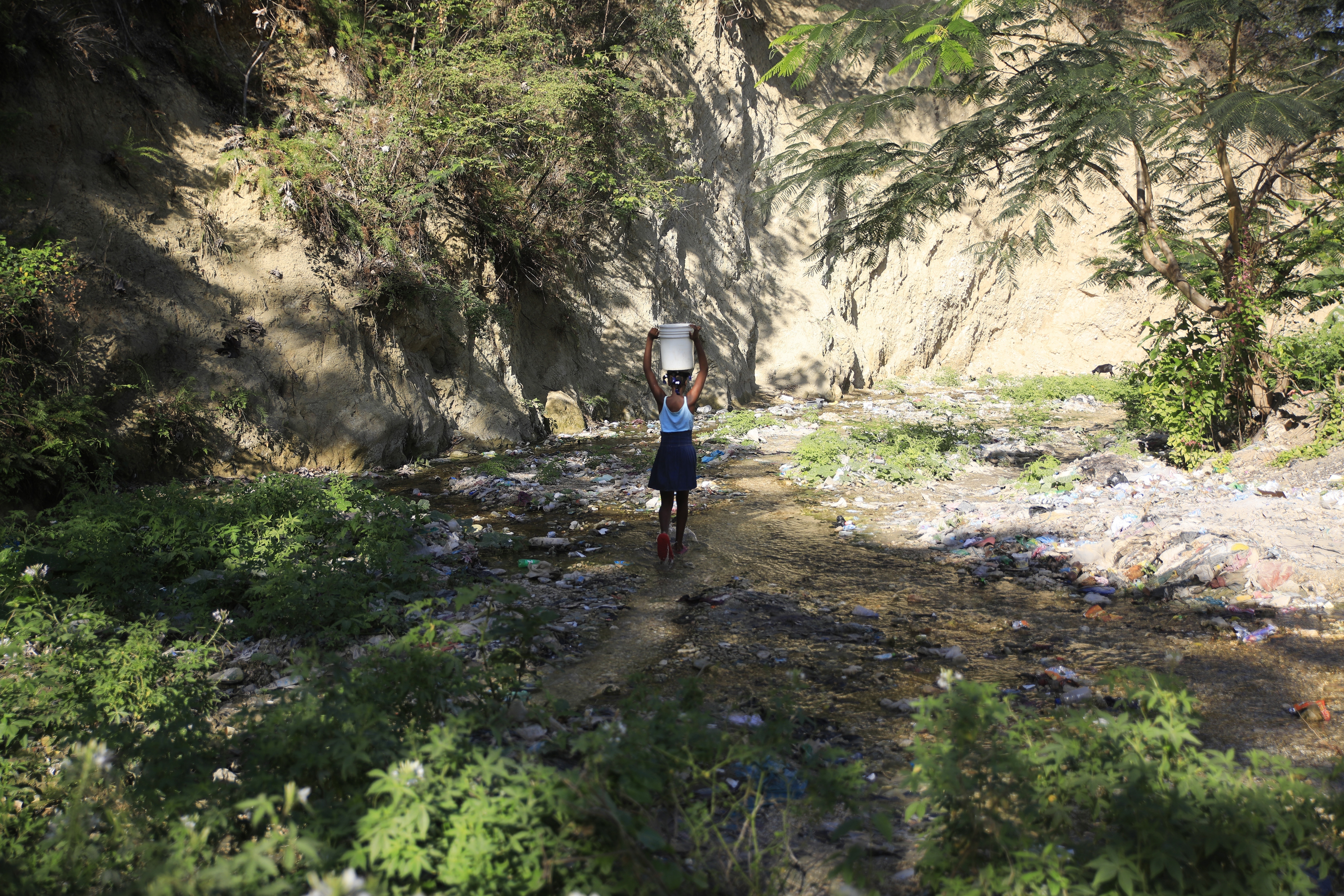 A youth without running water at home balances a bucket of water collected from a ravine in Port-au-Prince, Haiti