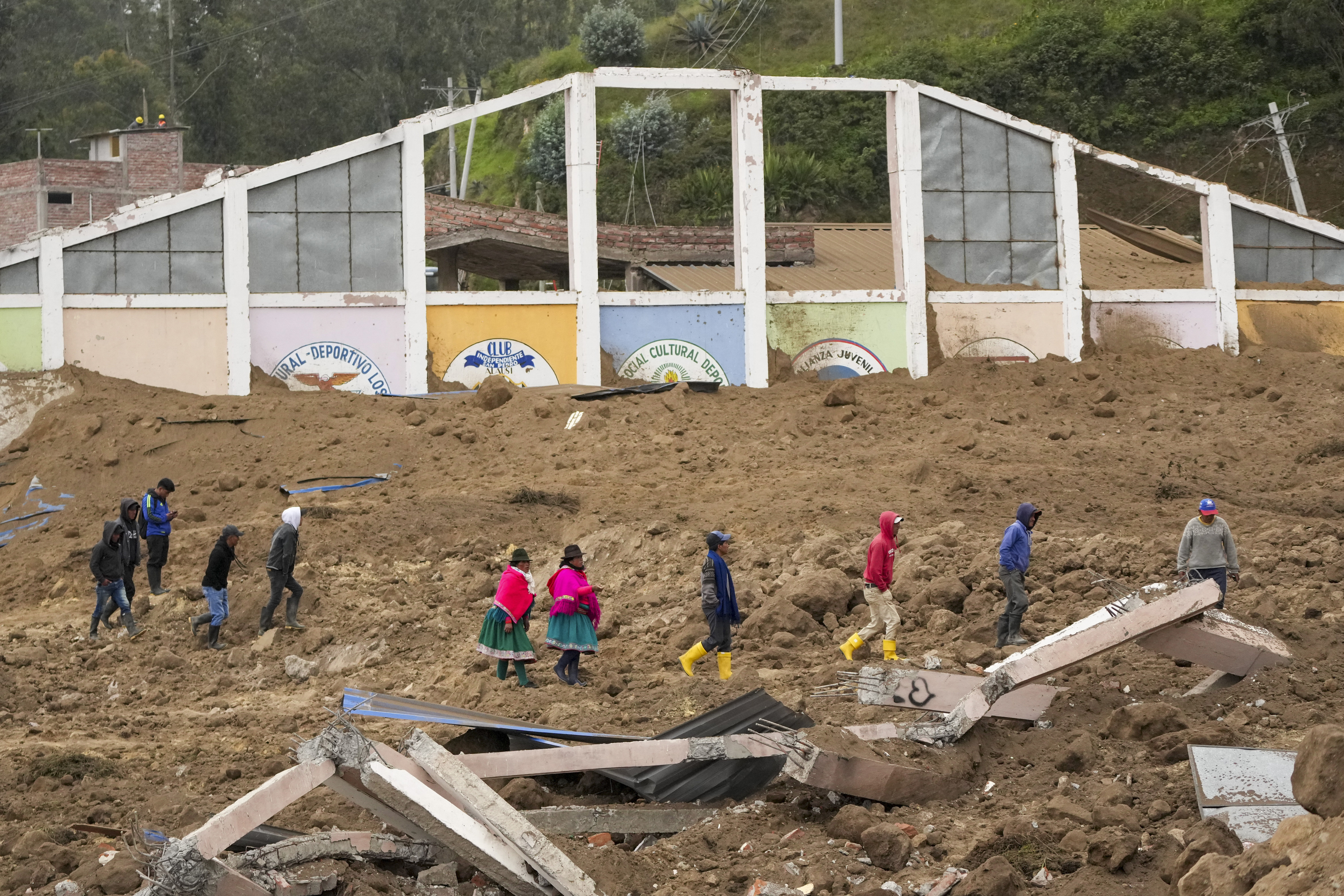 Residents walk past buildings destroyed by a deadly landslide that buried dozens of homes in Alausi, Ecuador