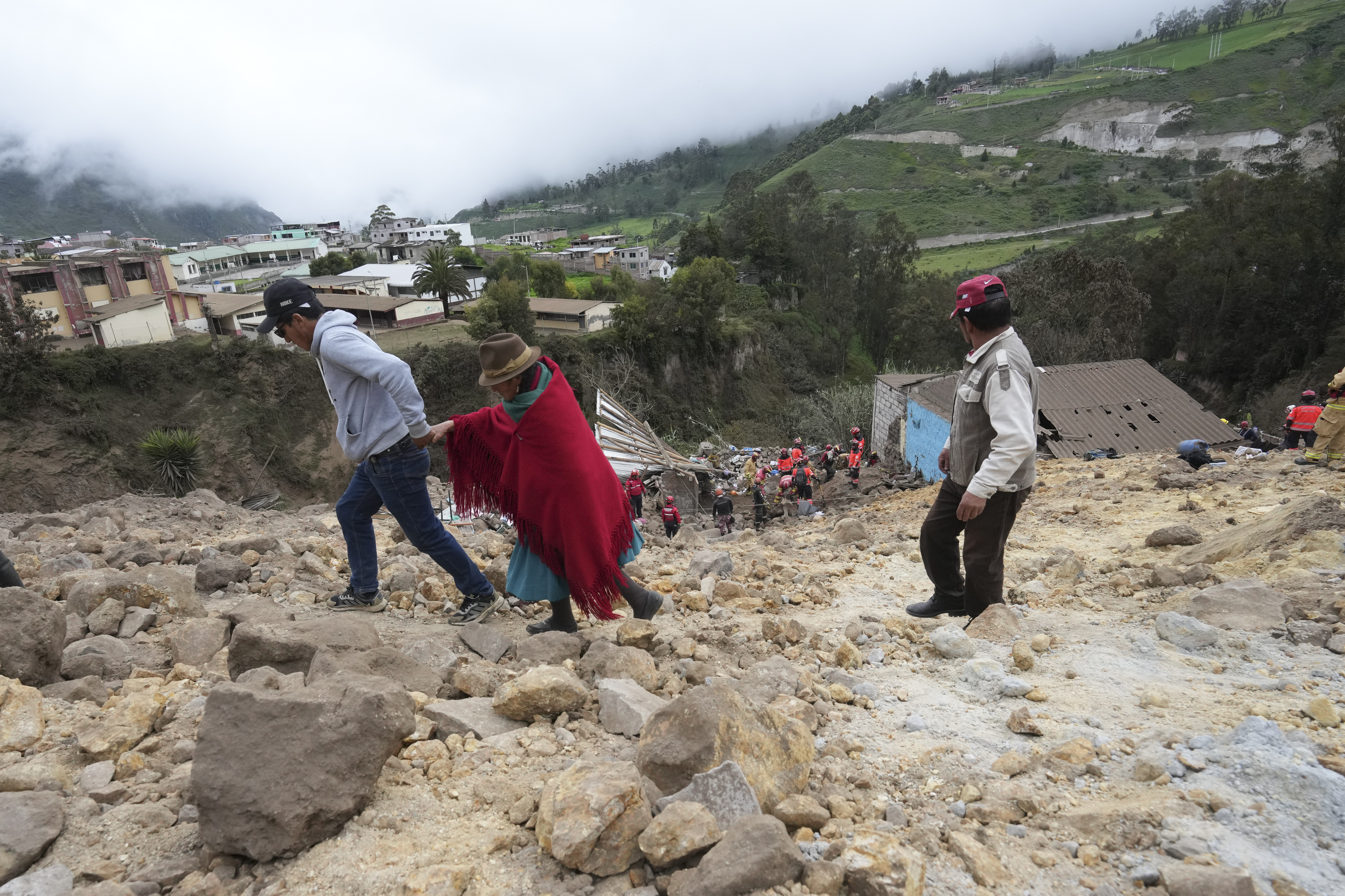 Residents walk on mud and stones after a deadly landslide buried dozens of homes in Alausi, Ecuador