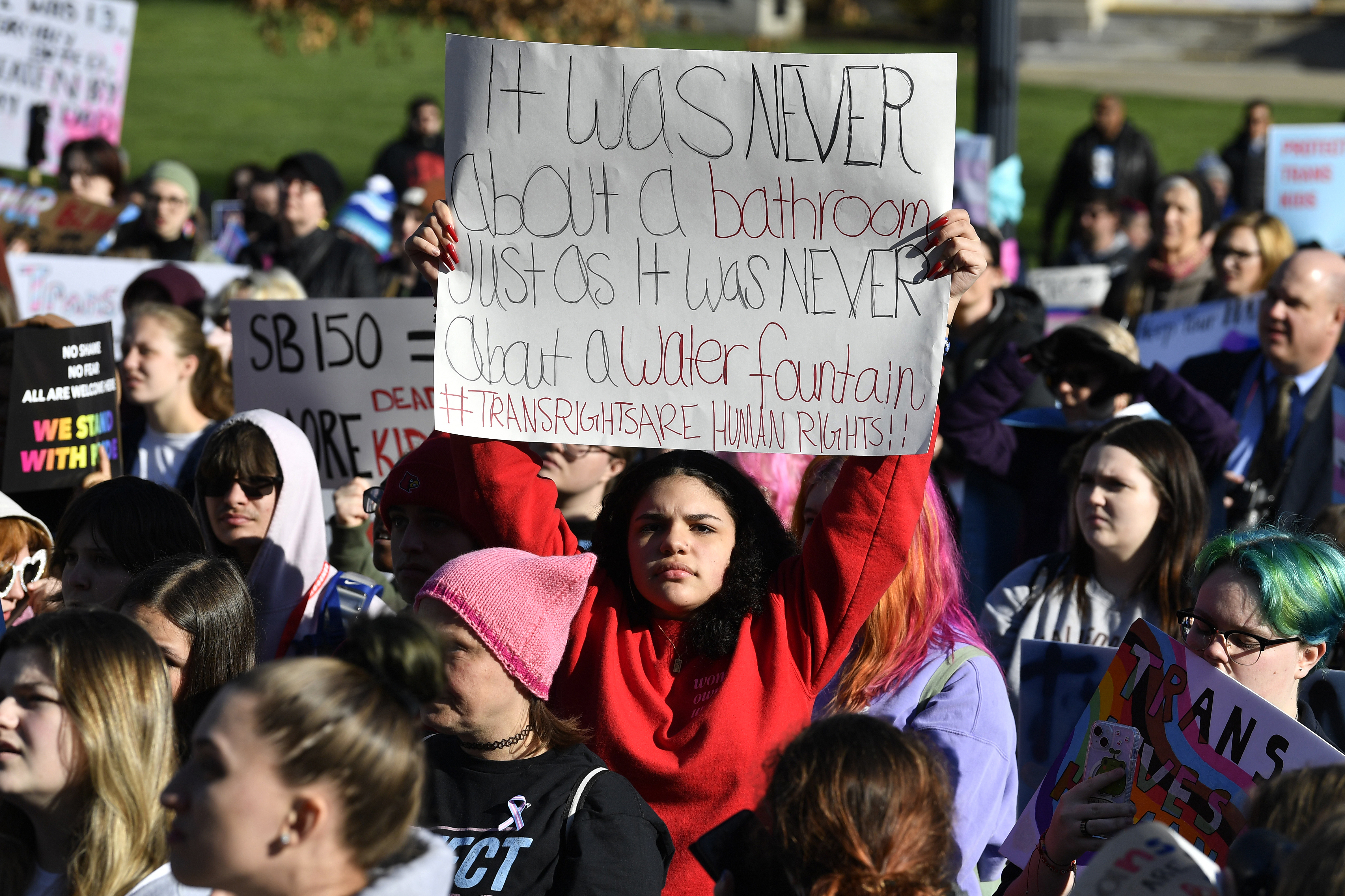 A woman holds up a sign that reads, "It was never about a bathroom just as it was never about a water fountain."