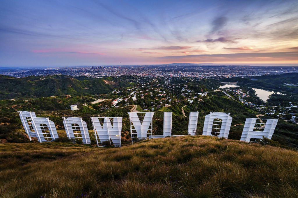 Sunset casts a pink glow over the Los Angeles skyline as seen from behind the famous Hollywood sign