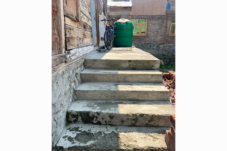 A photo of stairs going up outside with a bicycle and a tank on the top.
