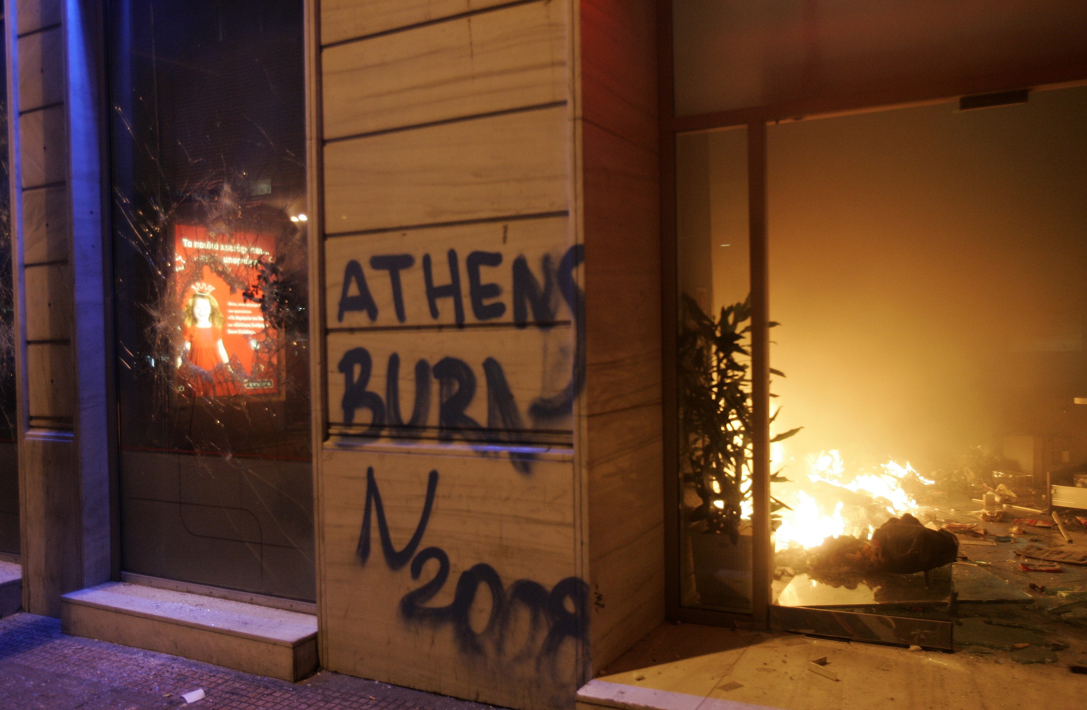 A bank marked with graffiti burns during riots in Athens December 8, 2008. Protesters set fire to a major department store in central Athens and torched the city's giant Christmas tree outside parliament as anti-government protests worsened. REUTERS/John Kolesidis (GREECE)