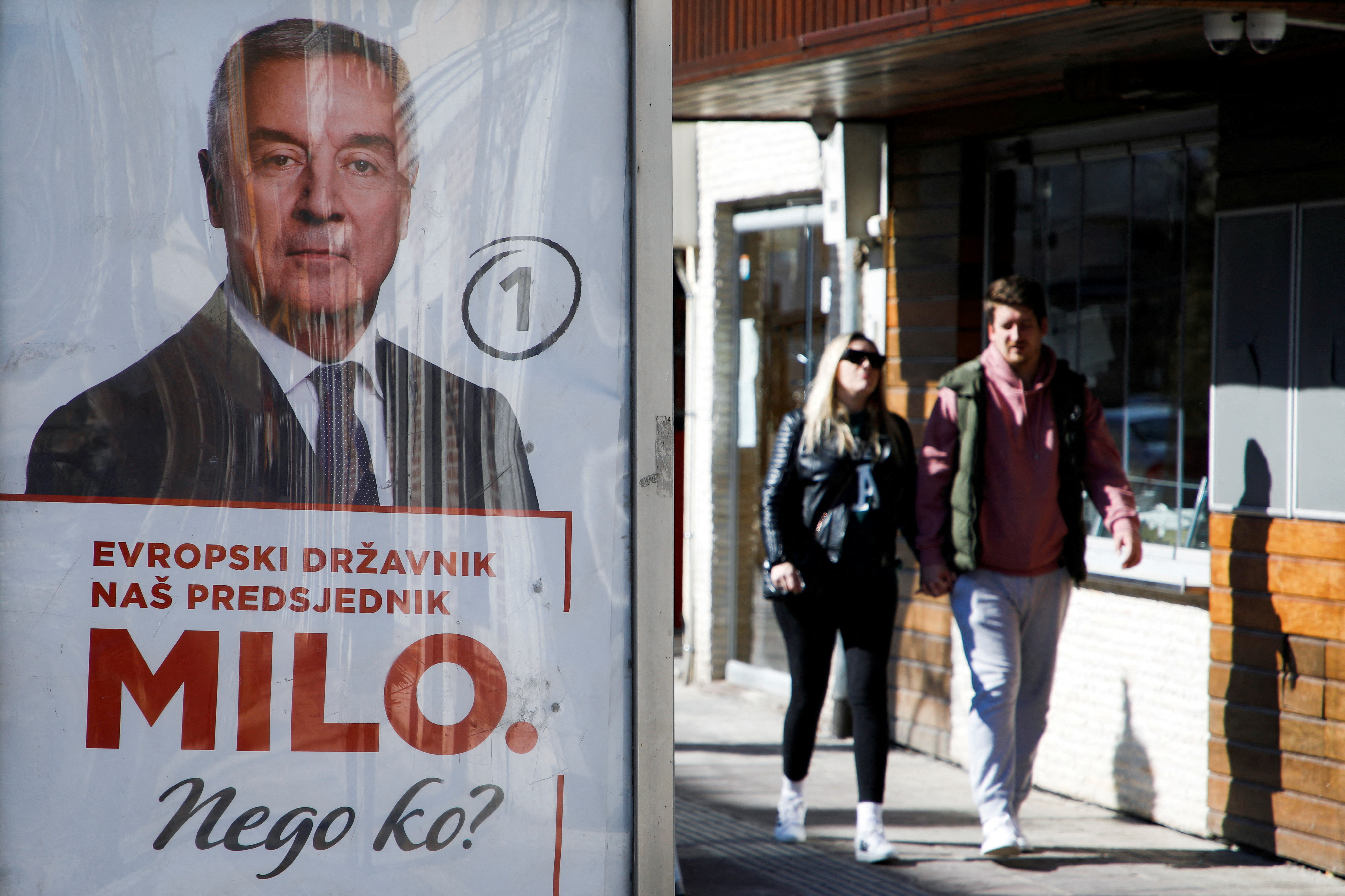 FILE PHOTO: A couple walks behind a pre-election poster of long-time incumbent Milo Djukanovic in Podgorica, Montenegro