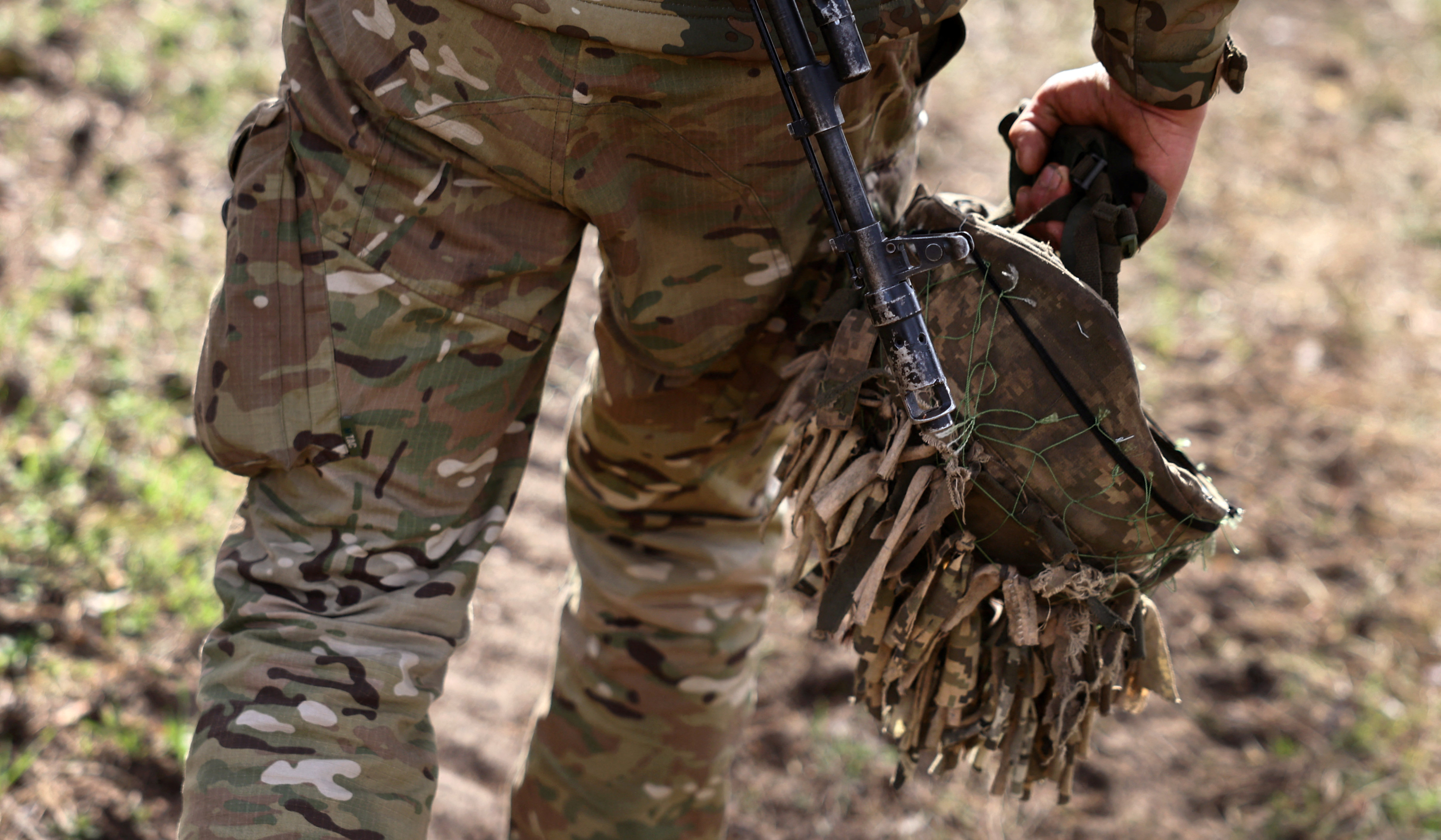 A Ukrainian soldier takes off his helmet after incoming shelling on the frontline near Lyman. He is walking away from the camera and holding his helmet in his right hand.