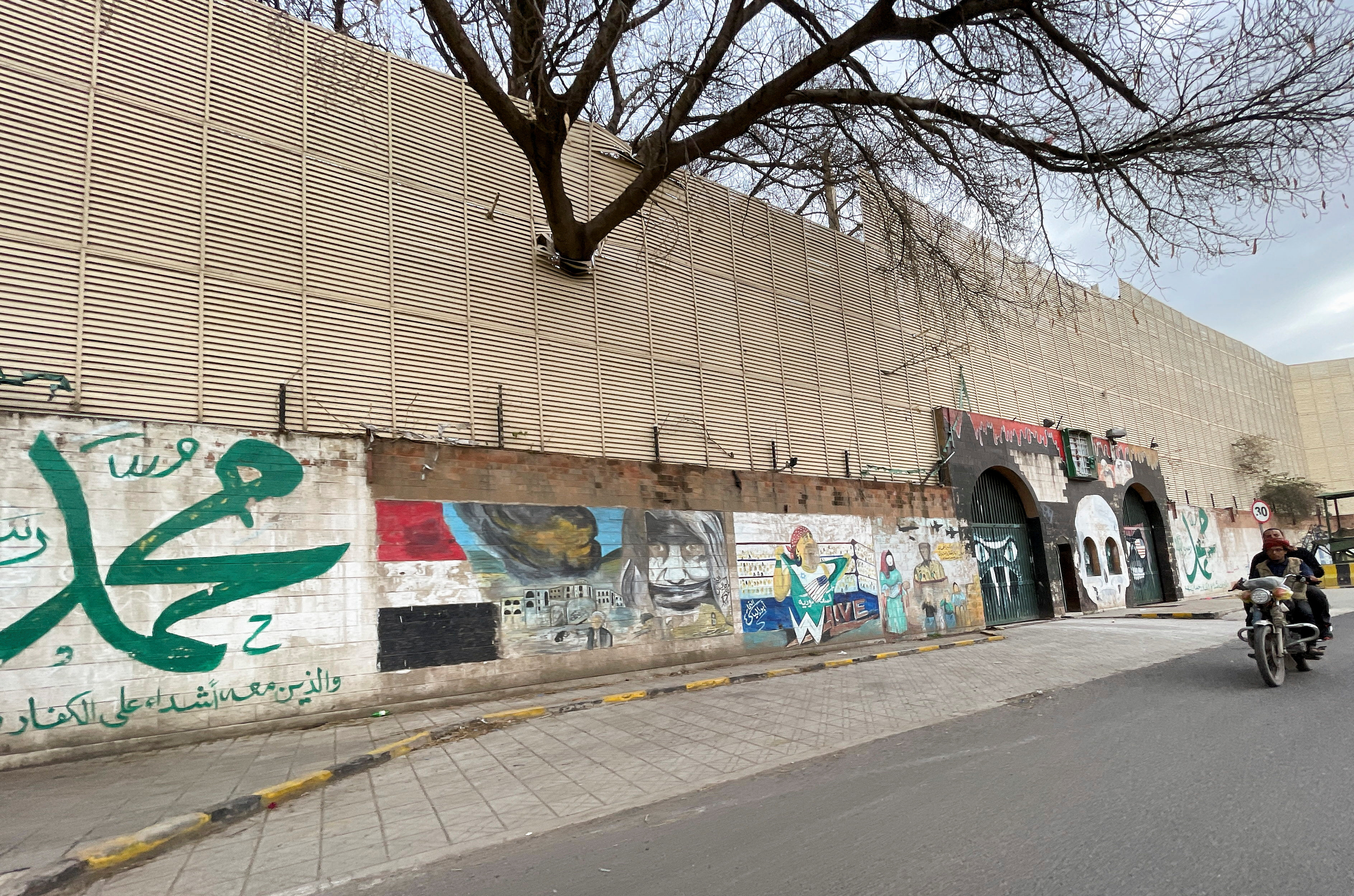People ride a motorbike past anti-Saudi graffiti on the gates and wall of the Saudi embassy