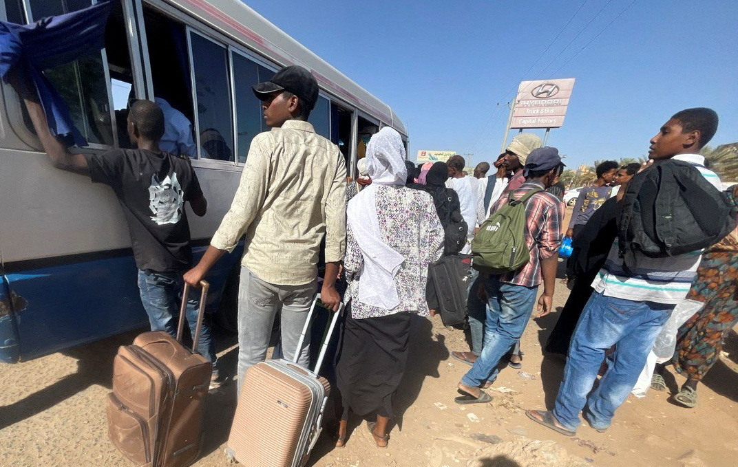 People crowding around a bus in Khartoum as they flee the city. They have suitcases with them.