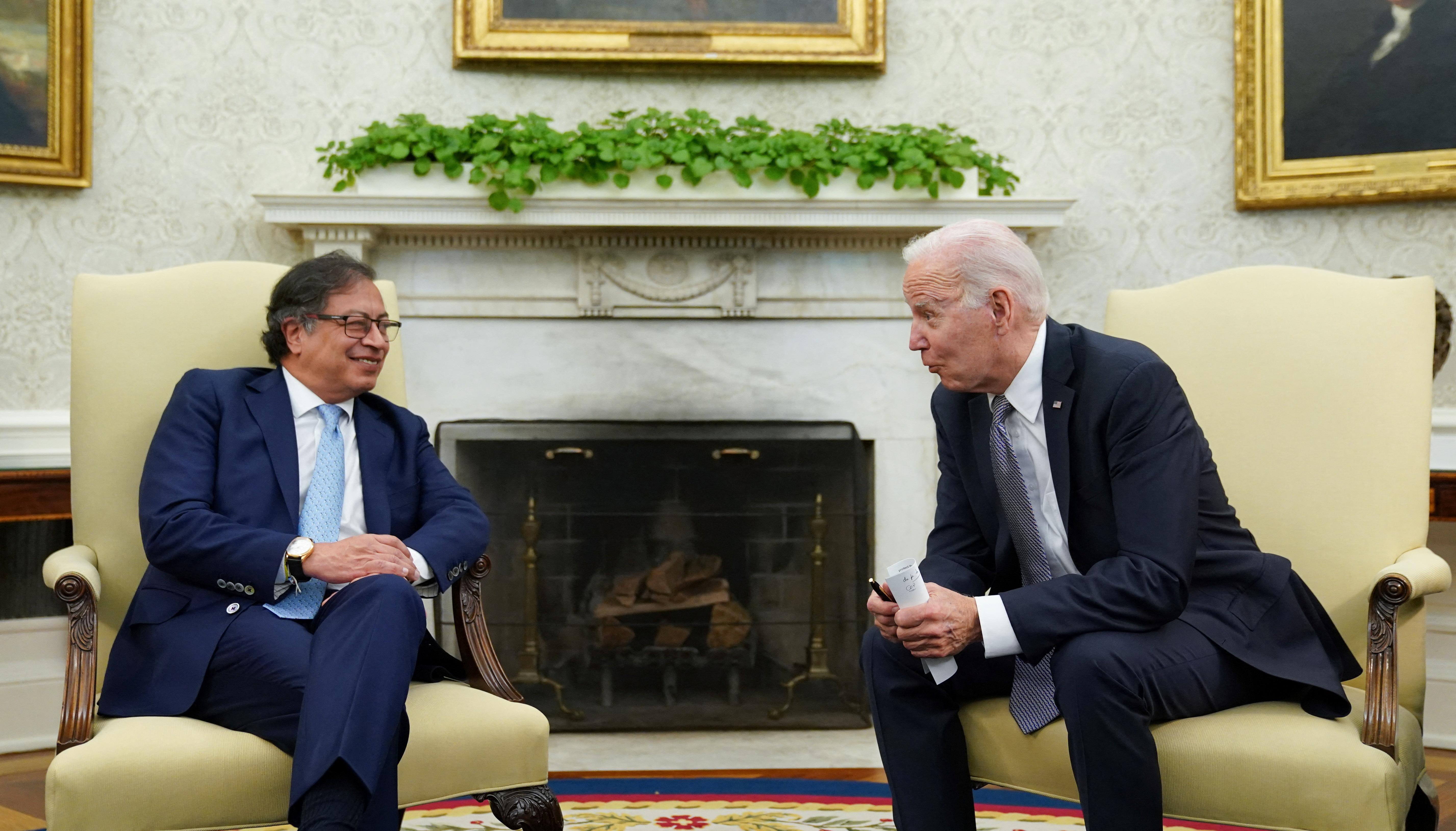 Joe Biden leans over from a beige chair to speak with Gustavo Petro in front of an empty fire place