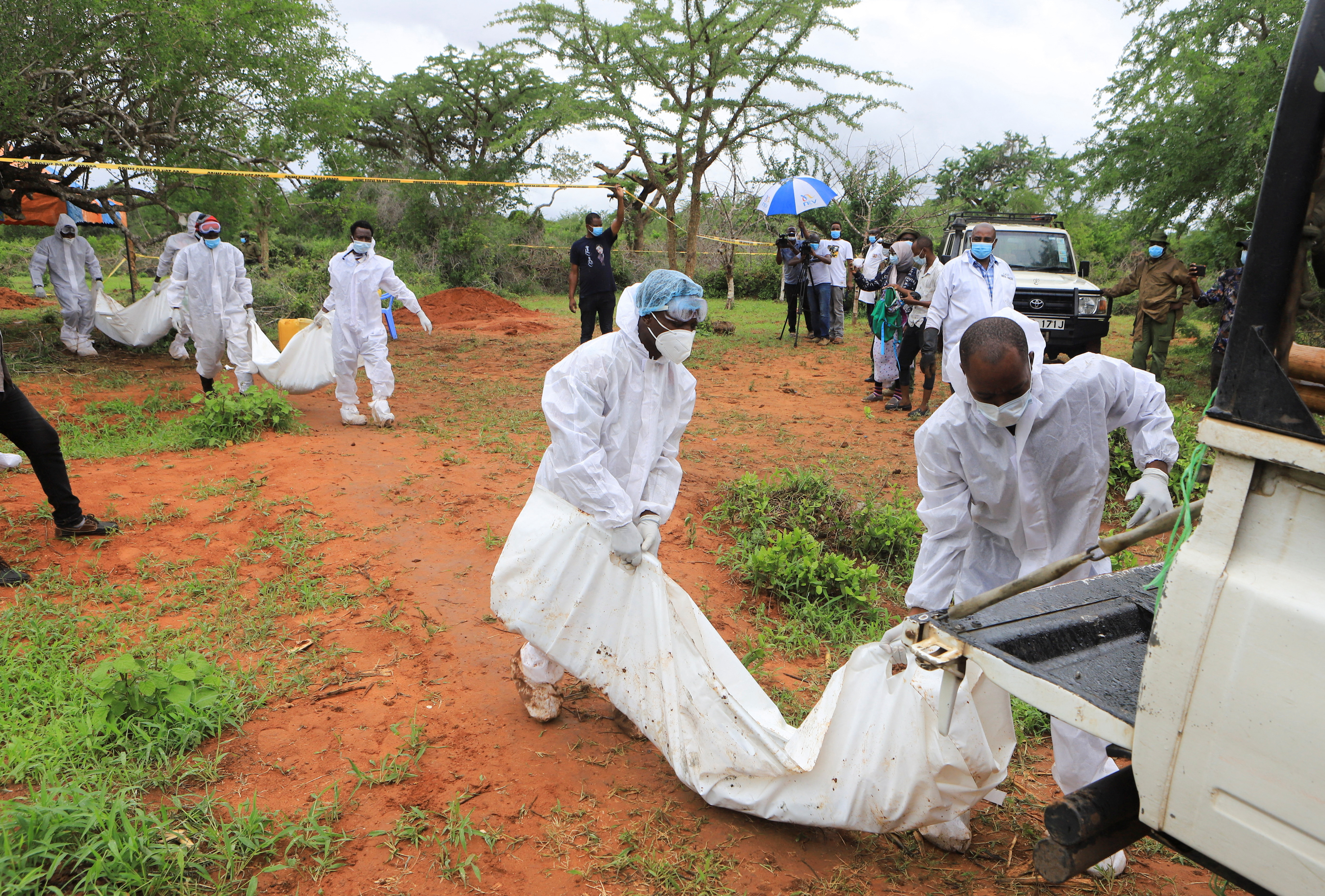 Kenyan forensic experts and homicide detectives, dressed in white personal protective equipment, carry the bodies of suspected members of a Christian cult to waiting vehicles as part of an investigation.
