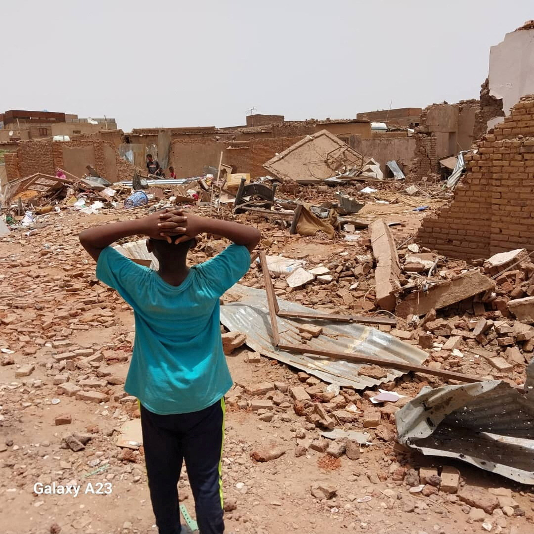 A person stands holding their hands over their heads as they look towards damaged buildings following clashes between the paramilitary Rapid Support Forces and the army in South Khartoum, Sudan.