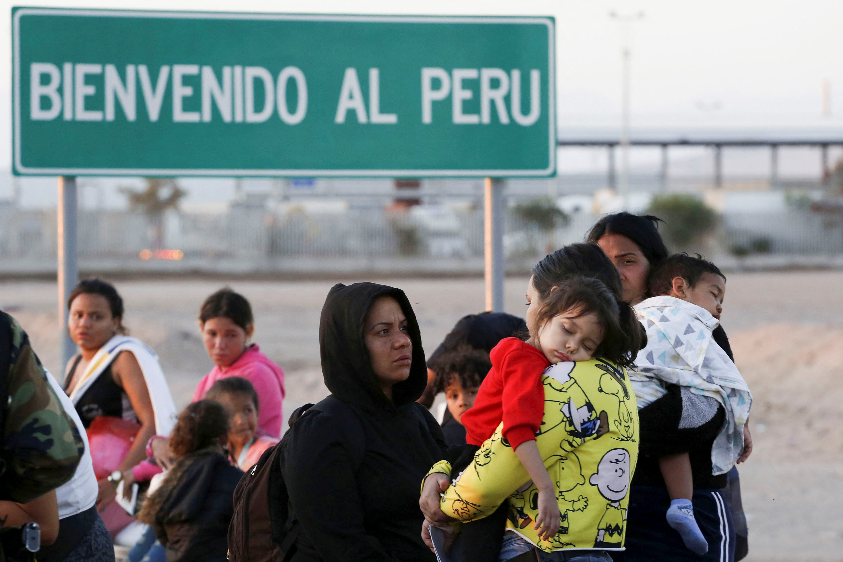 People stand next to a road sign reading 'Welcome to Peru'