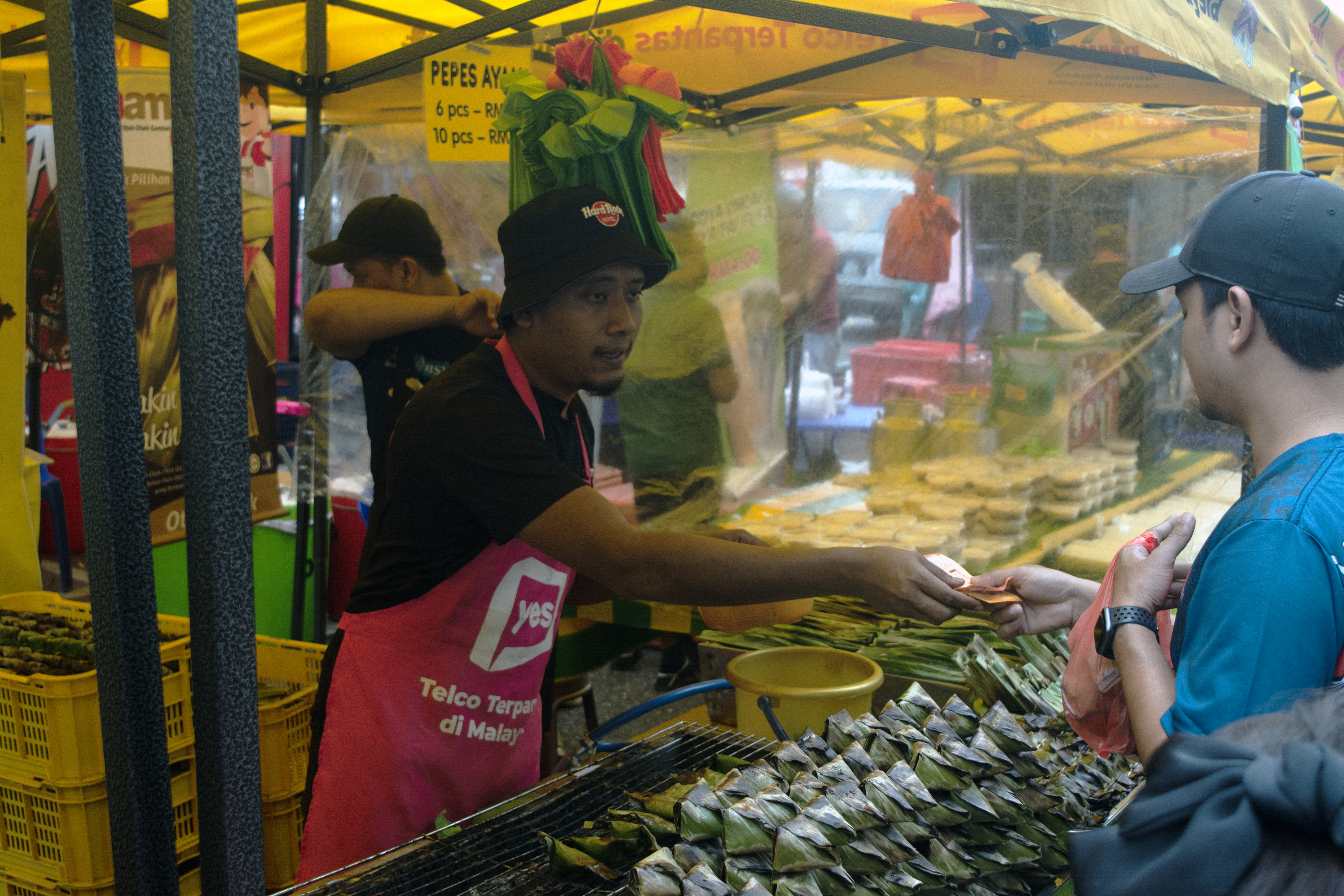 A man paying the vendor for the food he purchased that was packed in a plastic carry bag at a Ramadan bazaar in Malaysia.