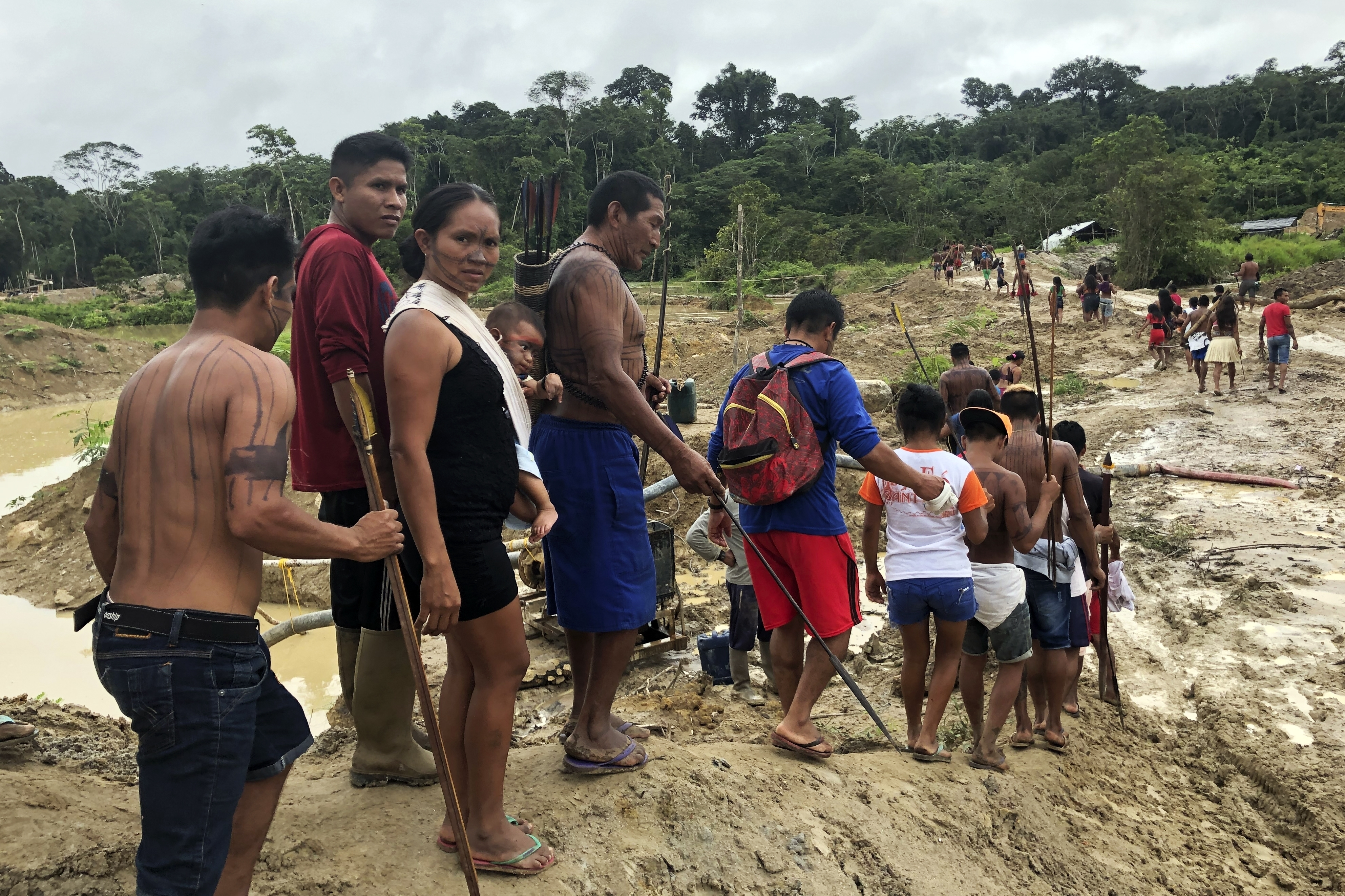 A line of people file downward into a muddy, deforested stretch of the Amazon rainforest.