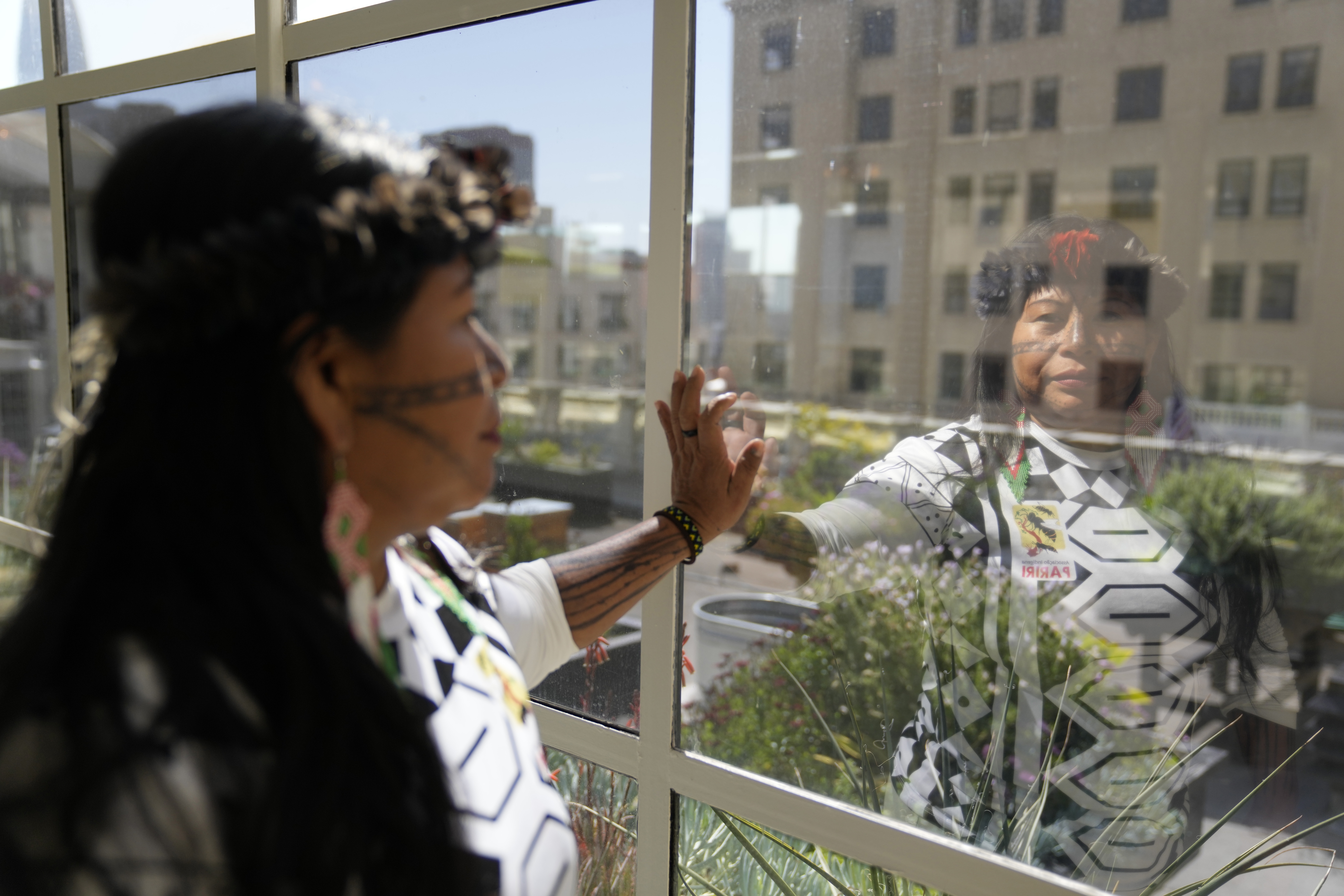 Alessandra Korap, winner of the 2023 Goldman Environmental Prize, looks out the window of a hotel, holding her hand up against the glass pane.