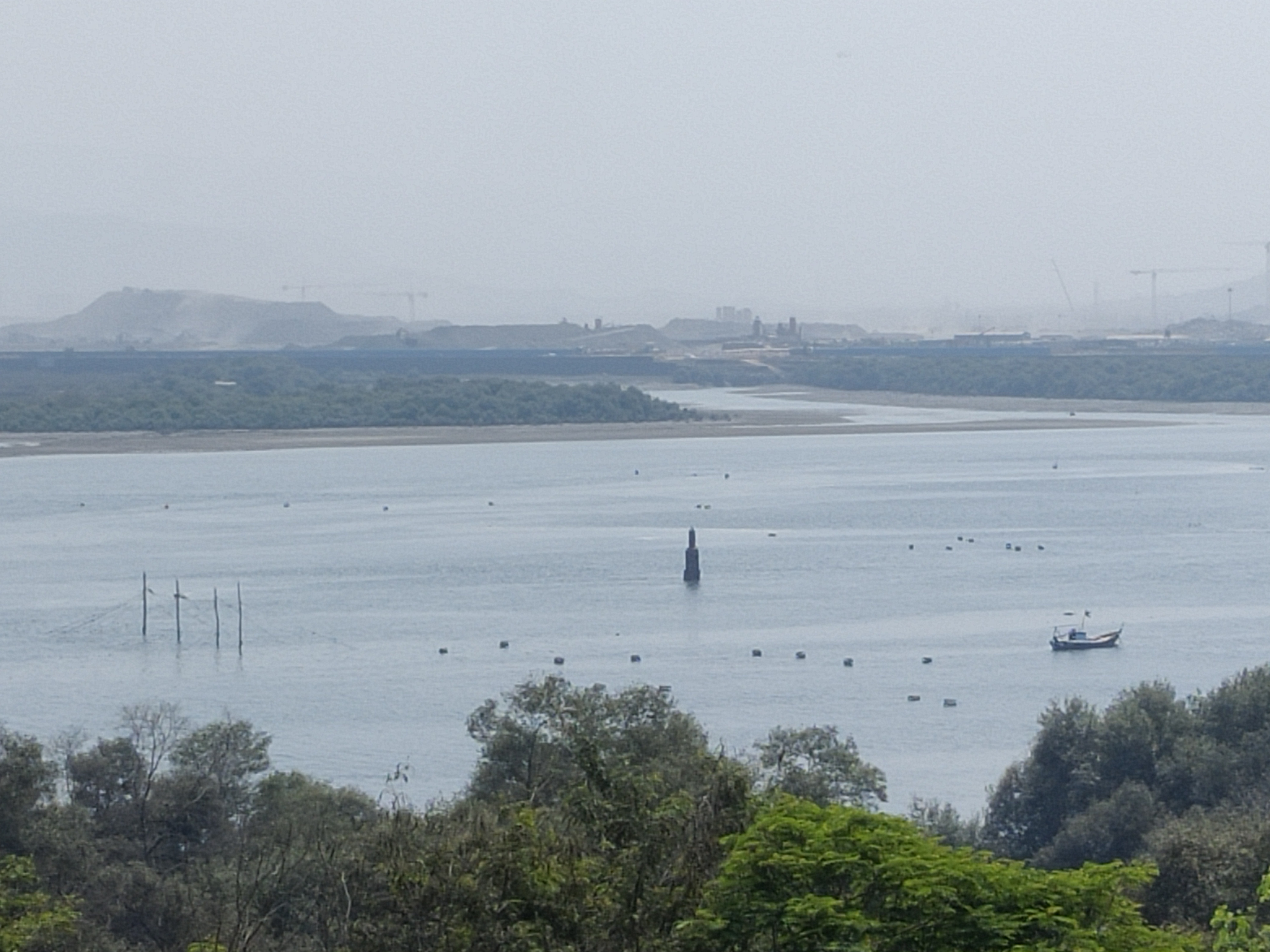 Skyline view of the construction of Navi Mumbai International Airport with water and vegetation in the foreground.