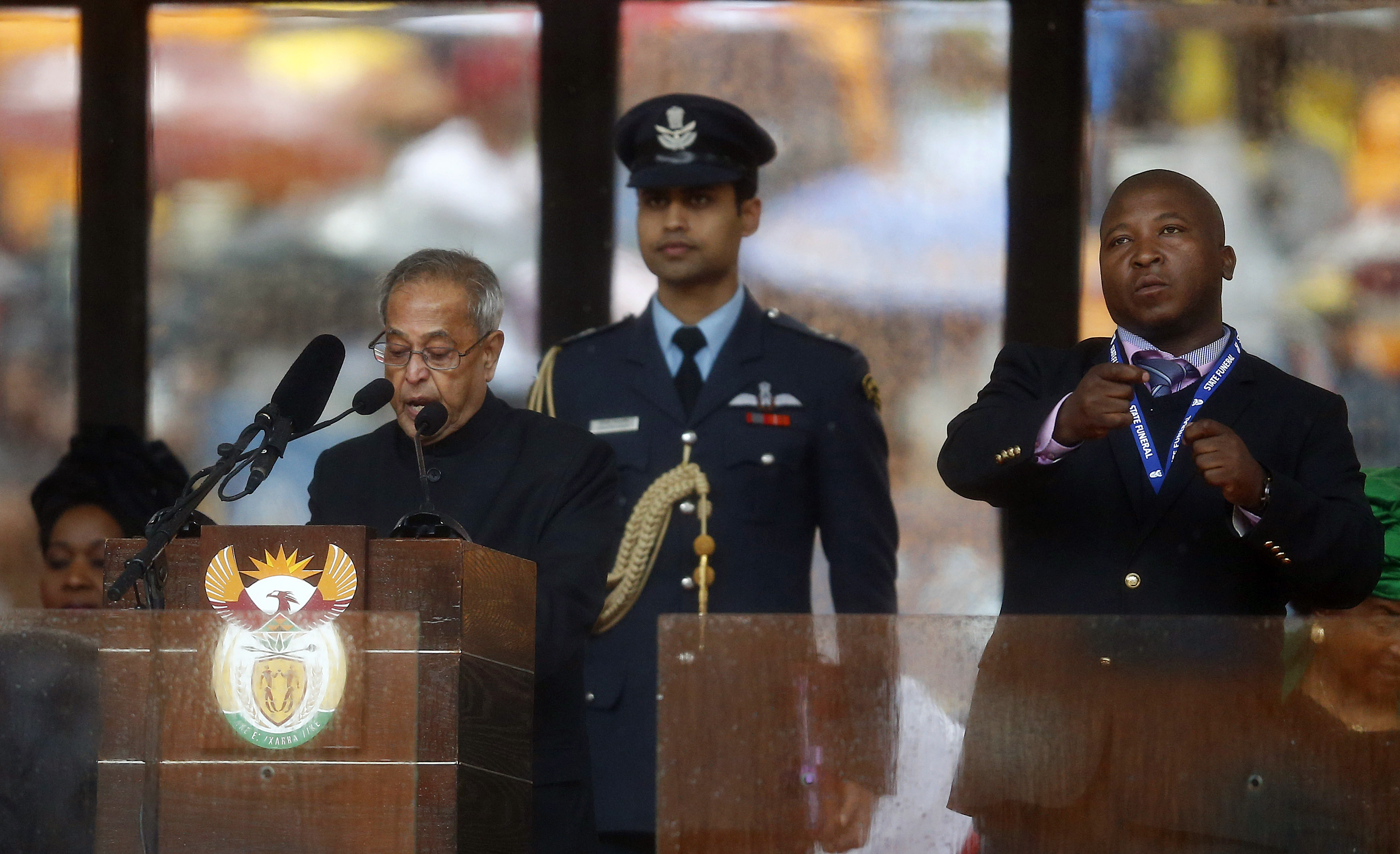 India's President Pranab Mukherjee speaks at the podium as a sign language interpreter (R) punches the air beside him during a memorial service for late South African President Nelson Mandela at the FNB soccer stadium in Johannesburg December 10, 2013. The fake sign language interpreter took to the stage during Tuesday's memorial for anti-apartheid leader Nelson Mandela, gesticulating gibberish before a global audience of millions and outraging deaf people across the world. Picture taken December 10. REUTERS/Kai Pfaffenbach (SOUTH AFRICA - Tags: POLITICS OBITUARY TPX IMAGES OF THE DAY)
