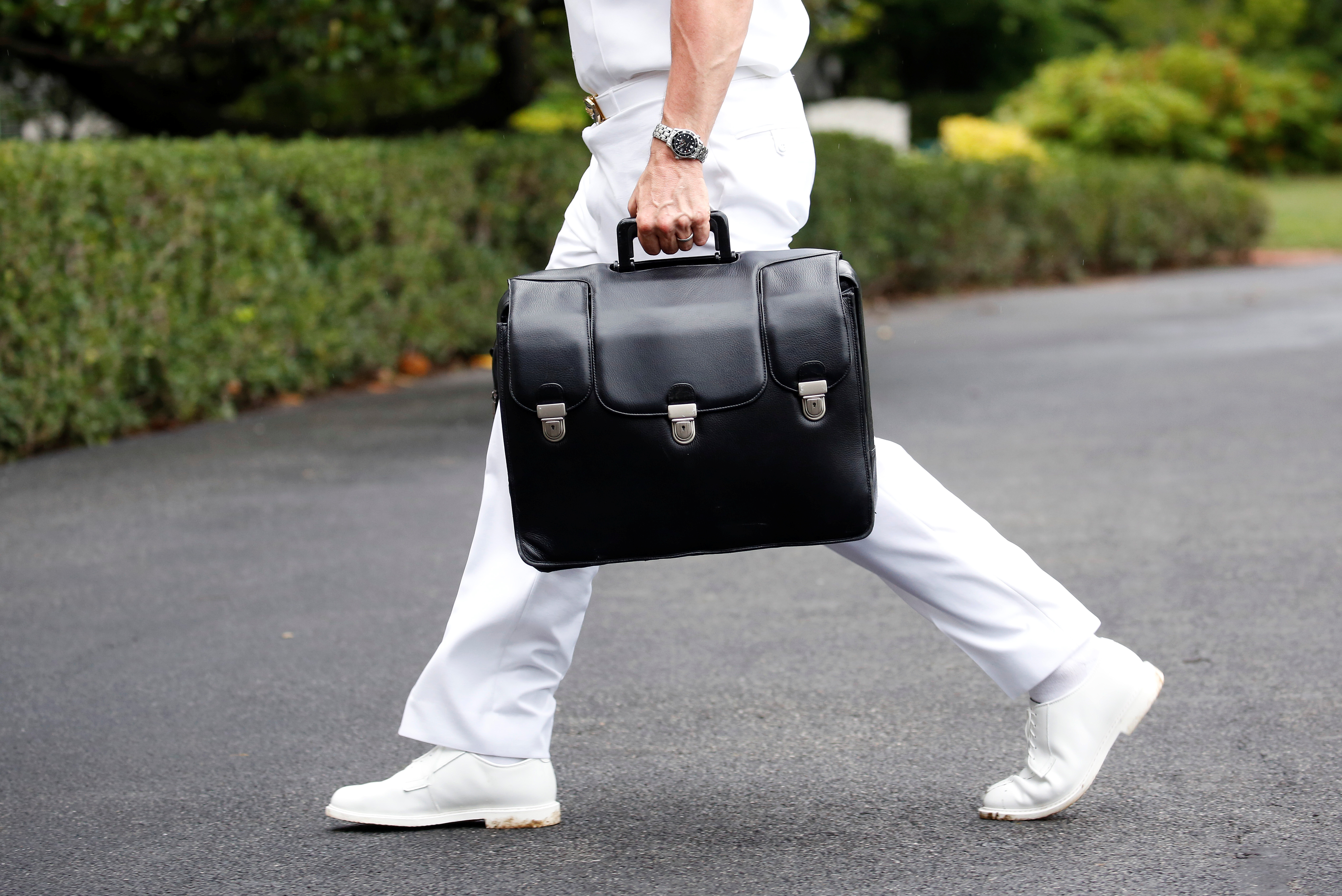 A military aide walking with the case holding the US nuclear codes. The case is black. The aide is walking right to left in the White House grounds and wearing a white uniform.