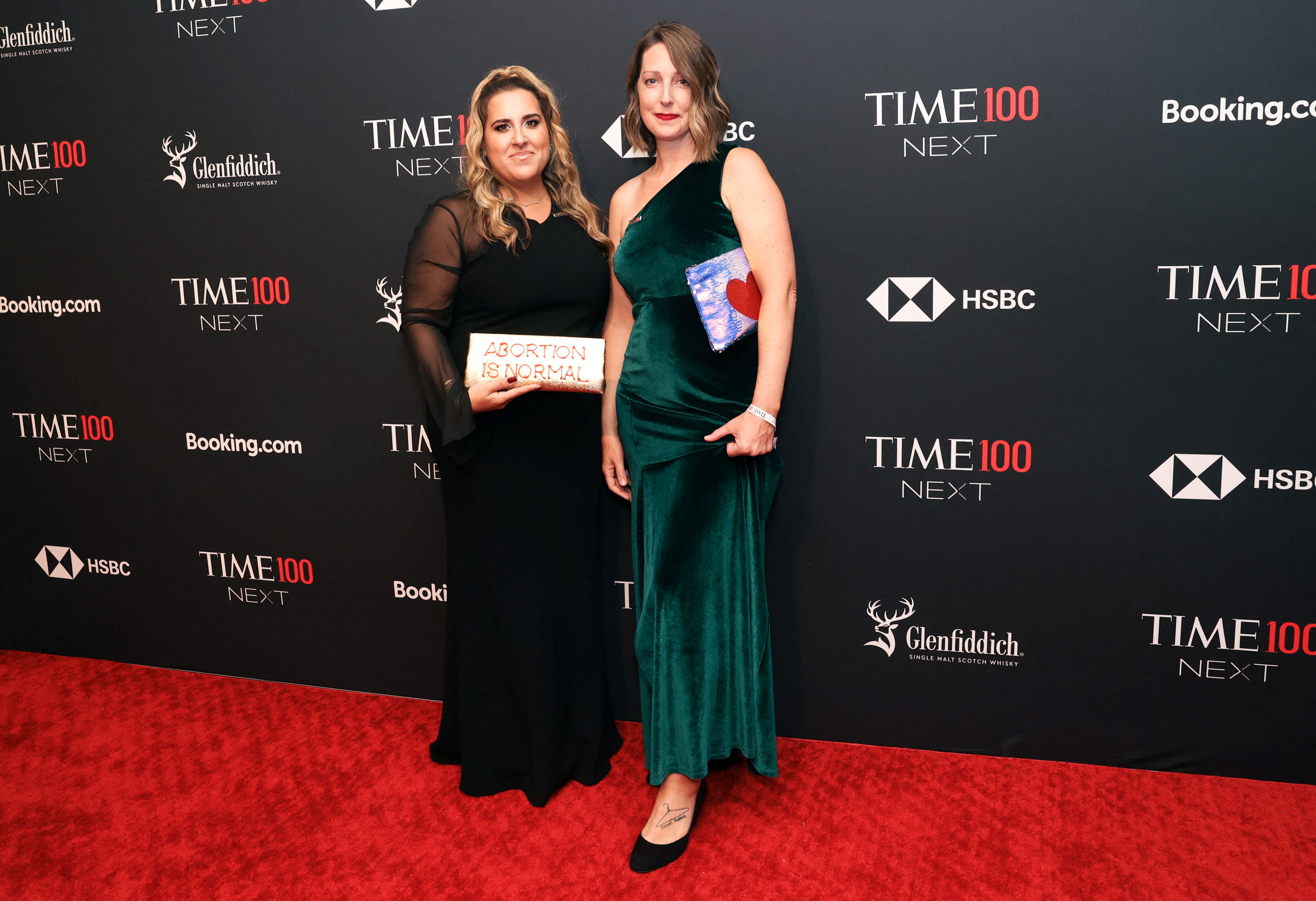 Two women in long gowns pose for photos on a red carpet.