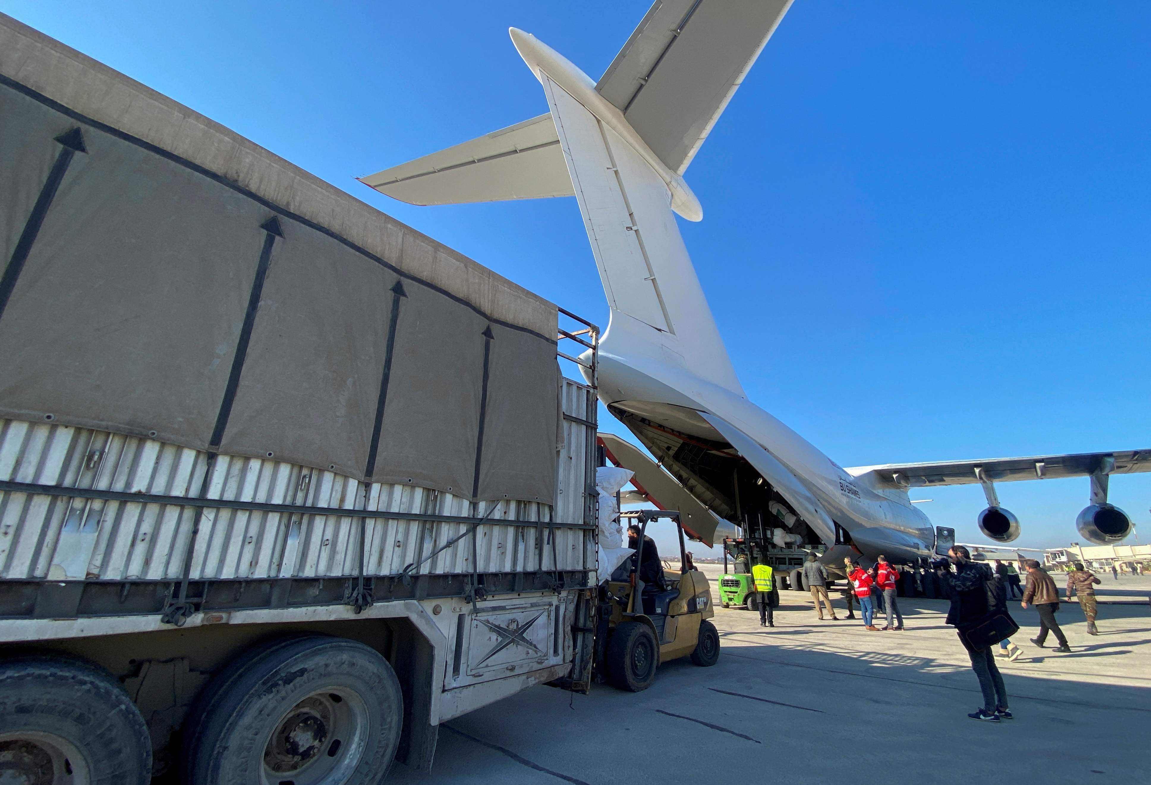 A cargo truck sits in front of a Saudi plane, whose cargo hold is open.