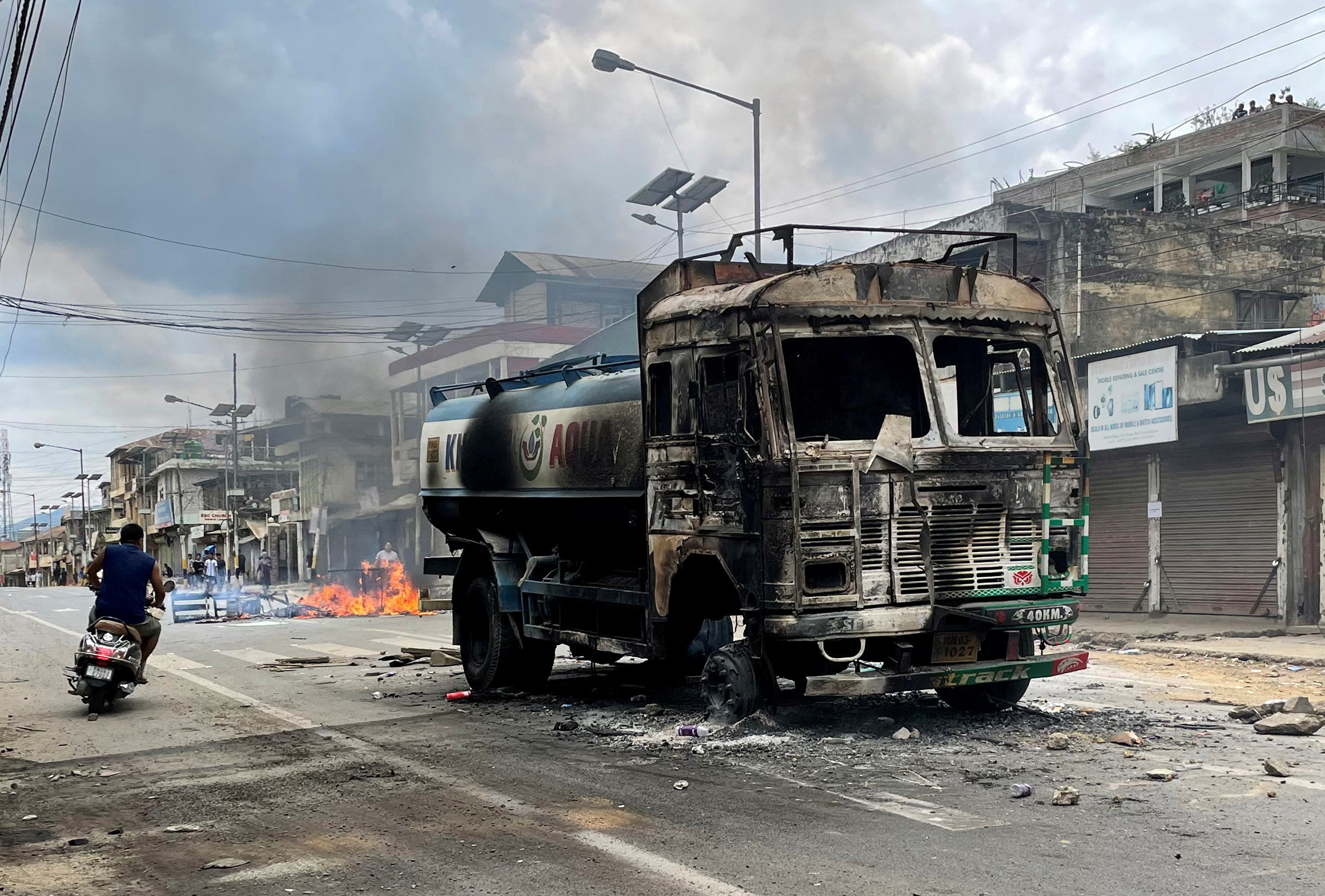 A scooterist rides past a damaged water tanker that was set afire during a protest by tribal groups in Churachandpur in the northeastern state of Manipur