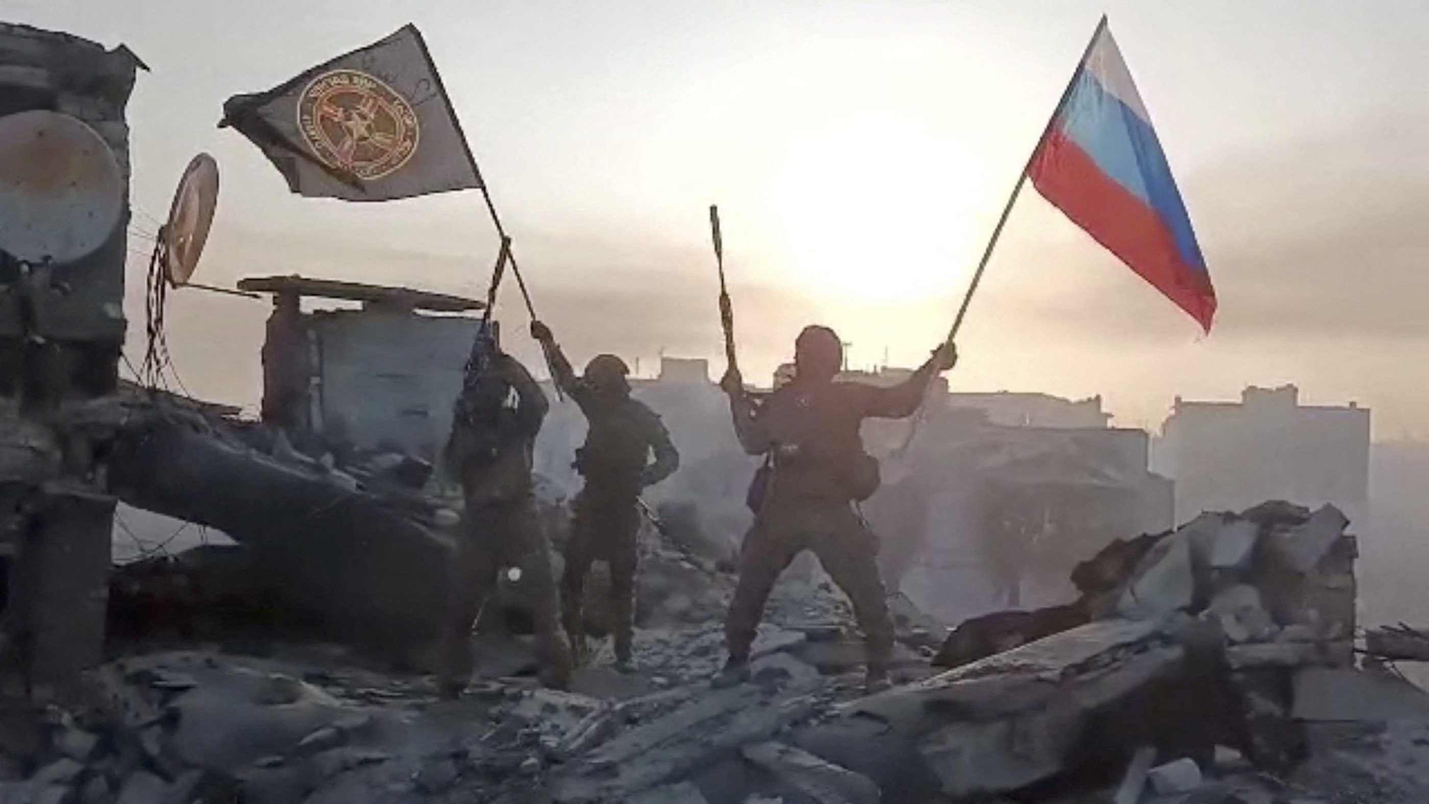 Mercenary fighters wave flags of Russia and the Wagner group on top of a building in an unidentified location.