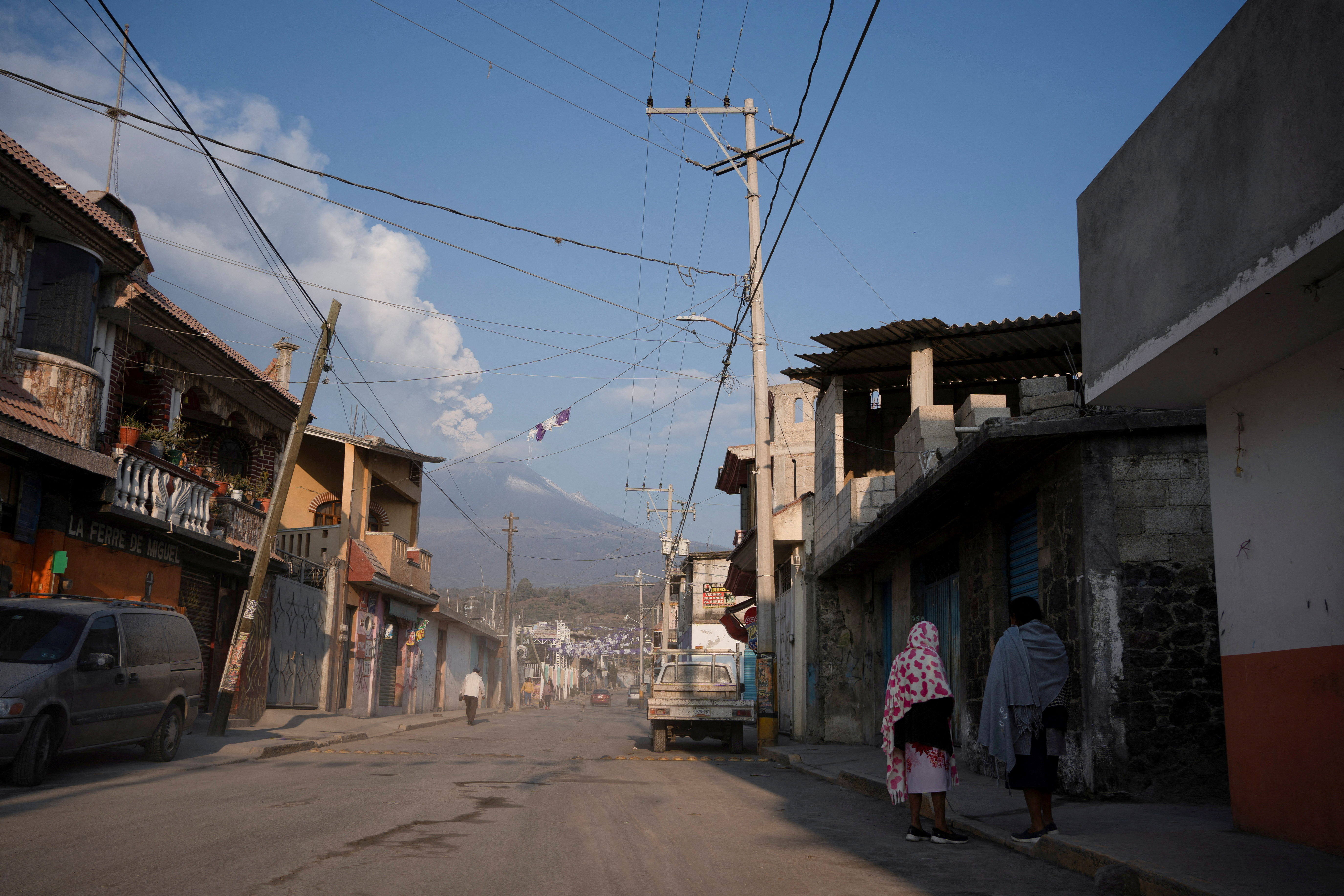 Residents chat on a street covered in volcanic ashes while the Popocatepetl volcano spews a column of steam and ashes, as seen from San Nicolas de los Ranchos, in Puebla state