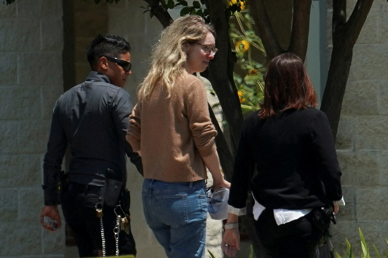 Elizabeth Holmes waking into the Federal Prison Camp in Bryan, Texas. She is wearing jeans and a sweater and looks relaxed.