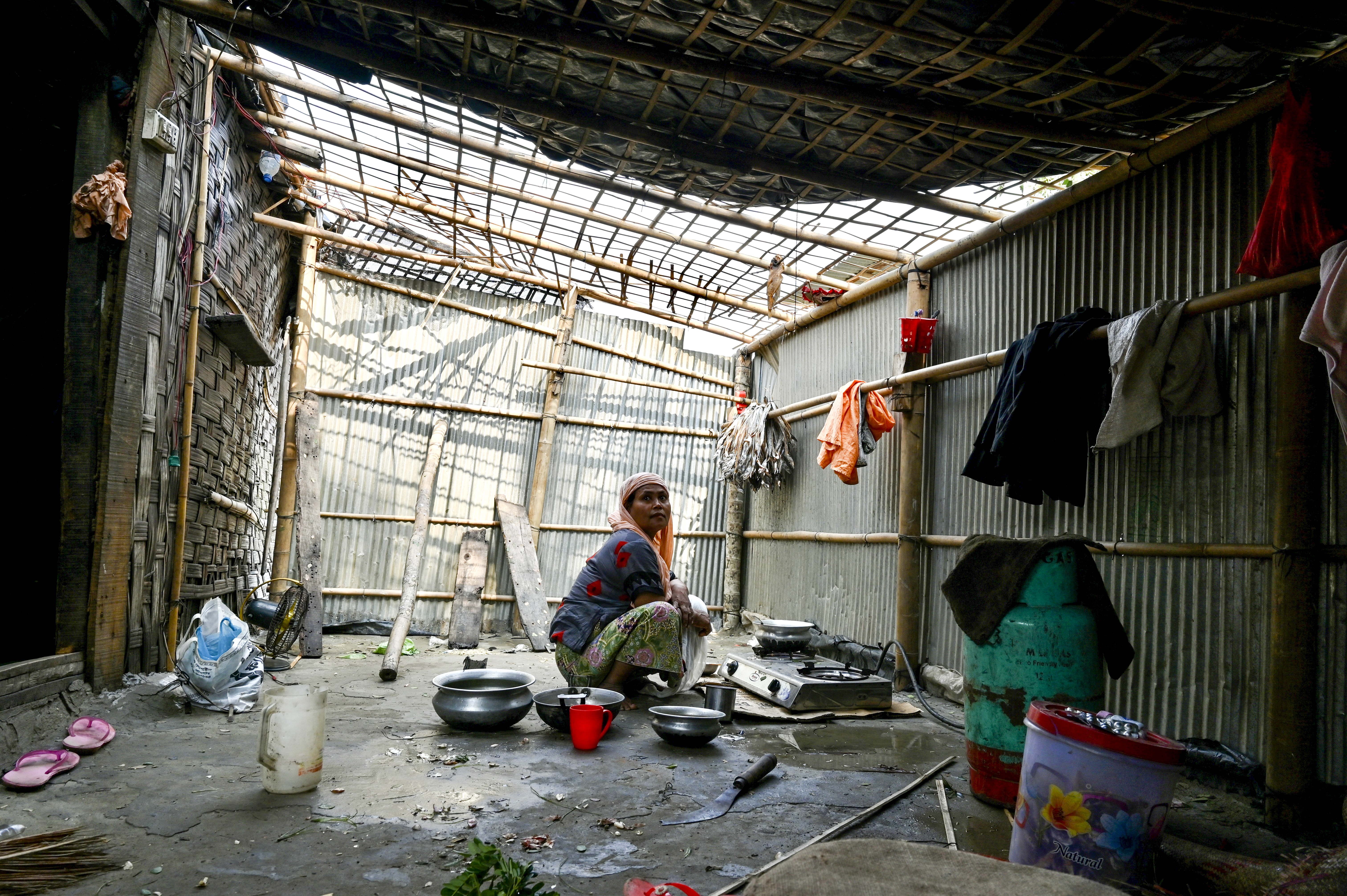 A woman cooks inside her house which was partially destroyed by cyclone Mocha, in Shahpori island on the outskirts of Teknaf
