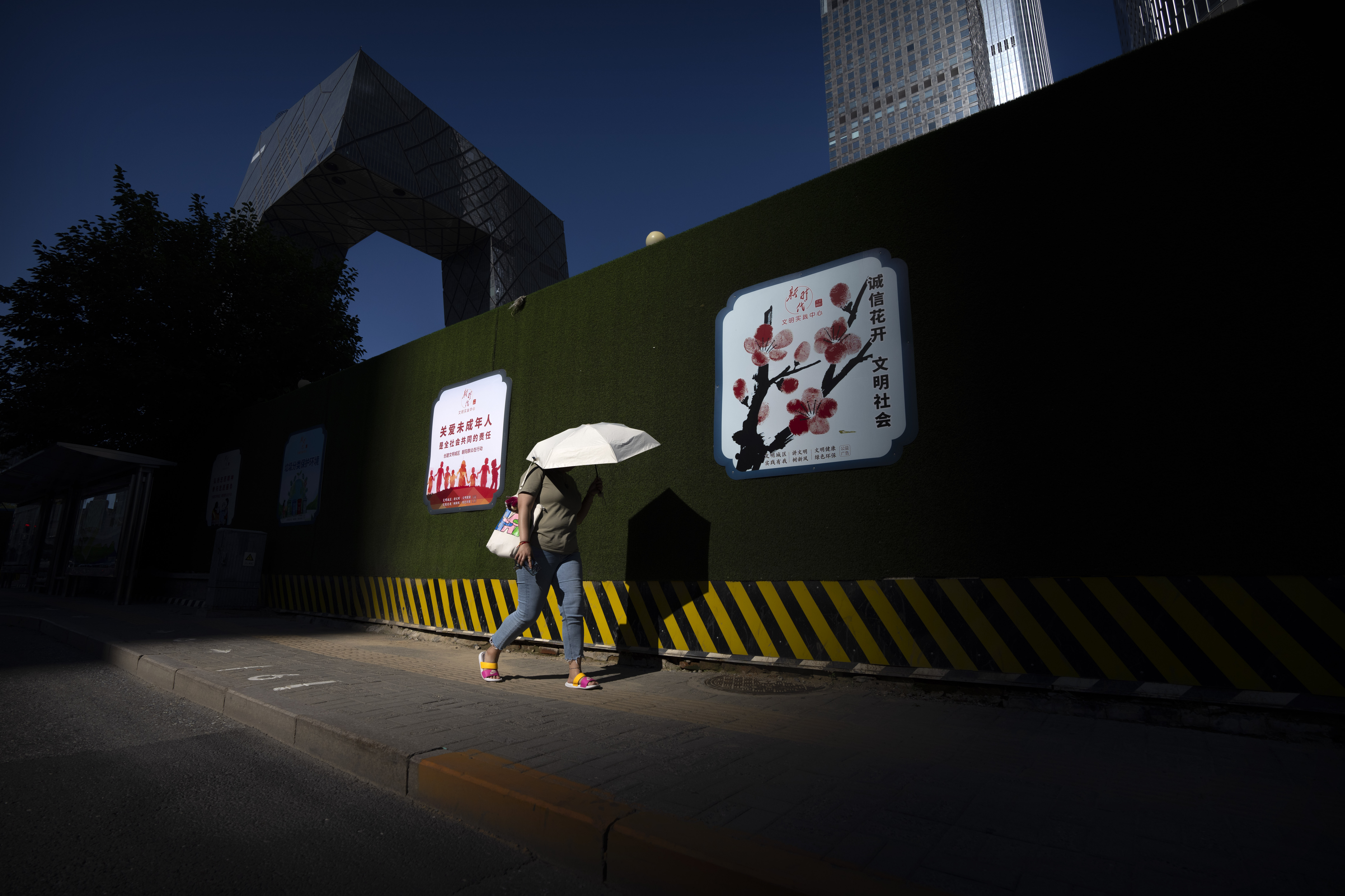 A woman uses an umbrella for shade as she walks through the central business district on an unseasonably warm day in Beijing, Thursday, July 14, 2022.