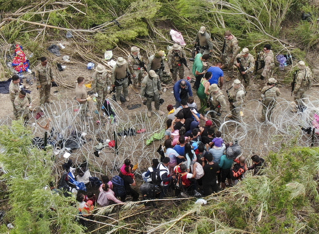 Migrants and US border forces divided by a razor wire fence