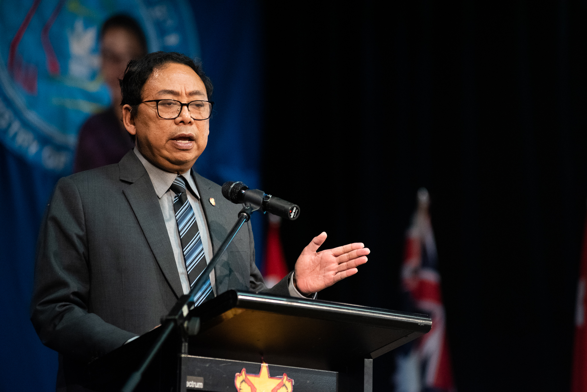 NUG Minister for Human Rights Aung Myo Min speaking at a lectern. He is wearing a suit and is making a point with his left hand.