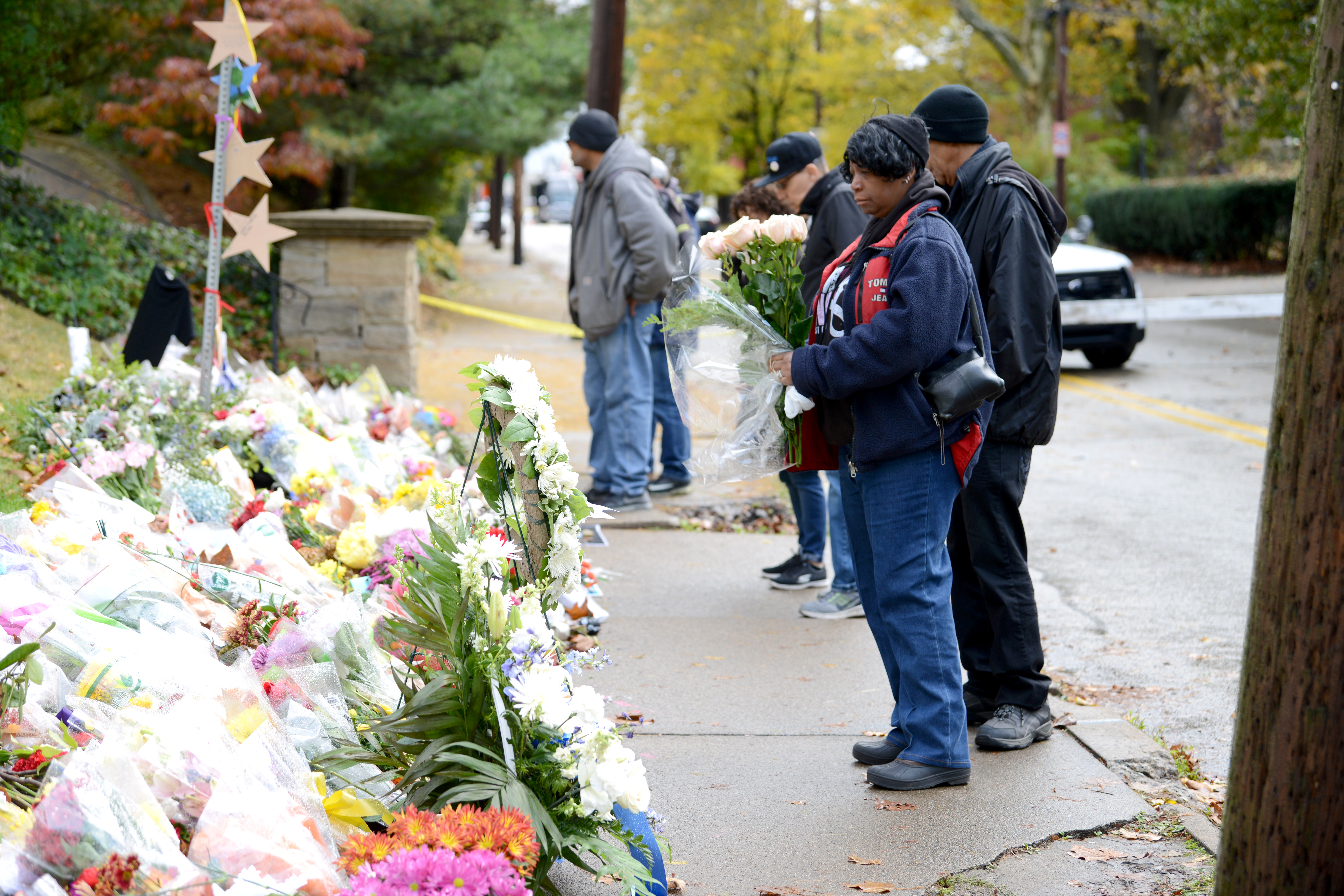 People stand in front of piles of flowers and signs — a memorial for the lives lost in Pittsburgh in October 2018