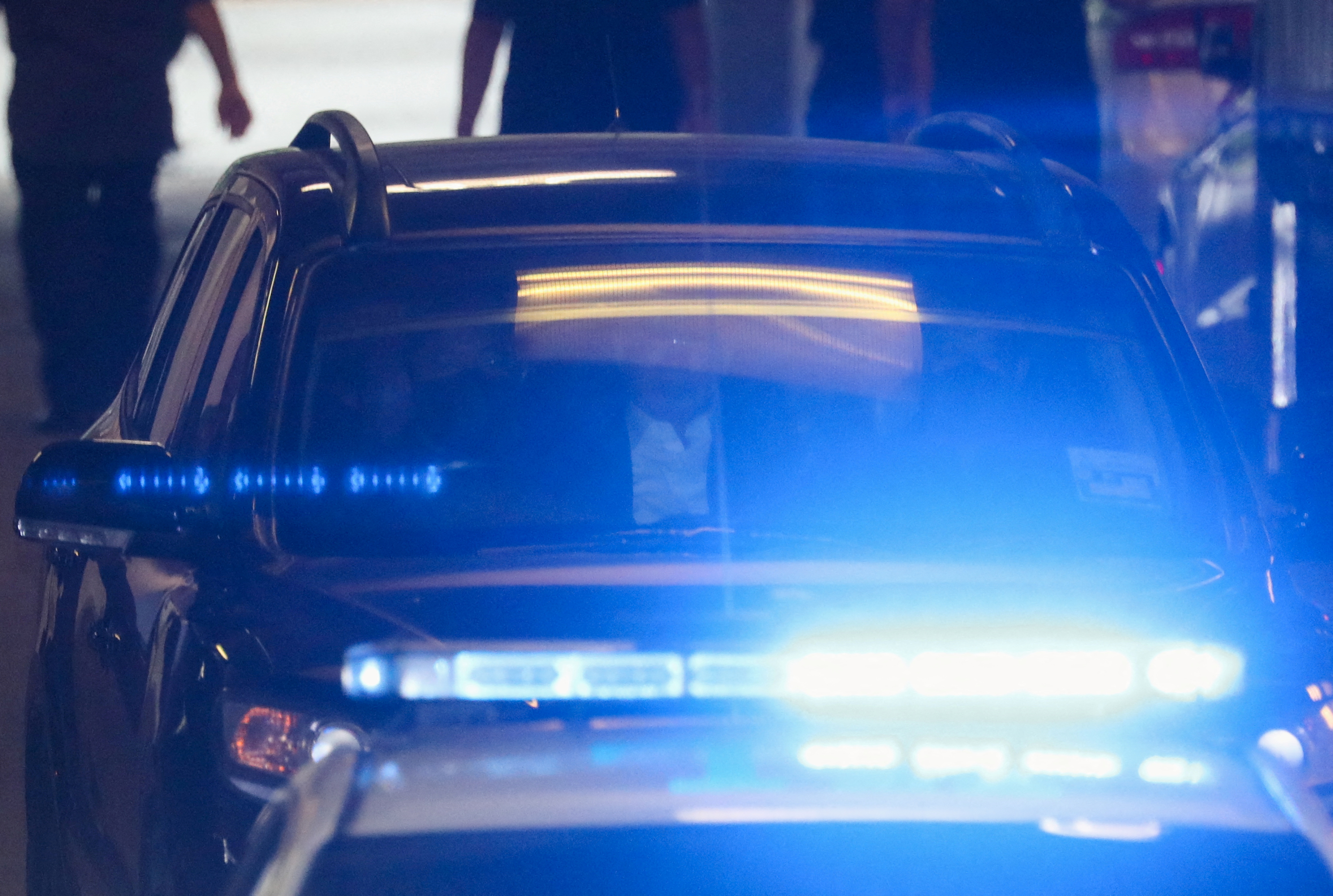 Najib Razak being taken to prison. He is in the back of an SUV being driven by two police officers. There is a flashing blue light