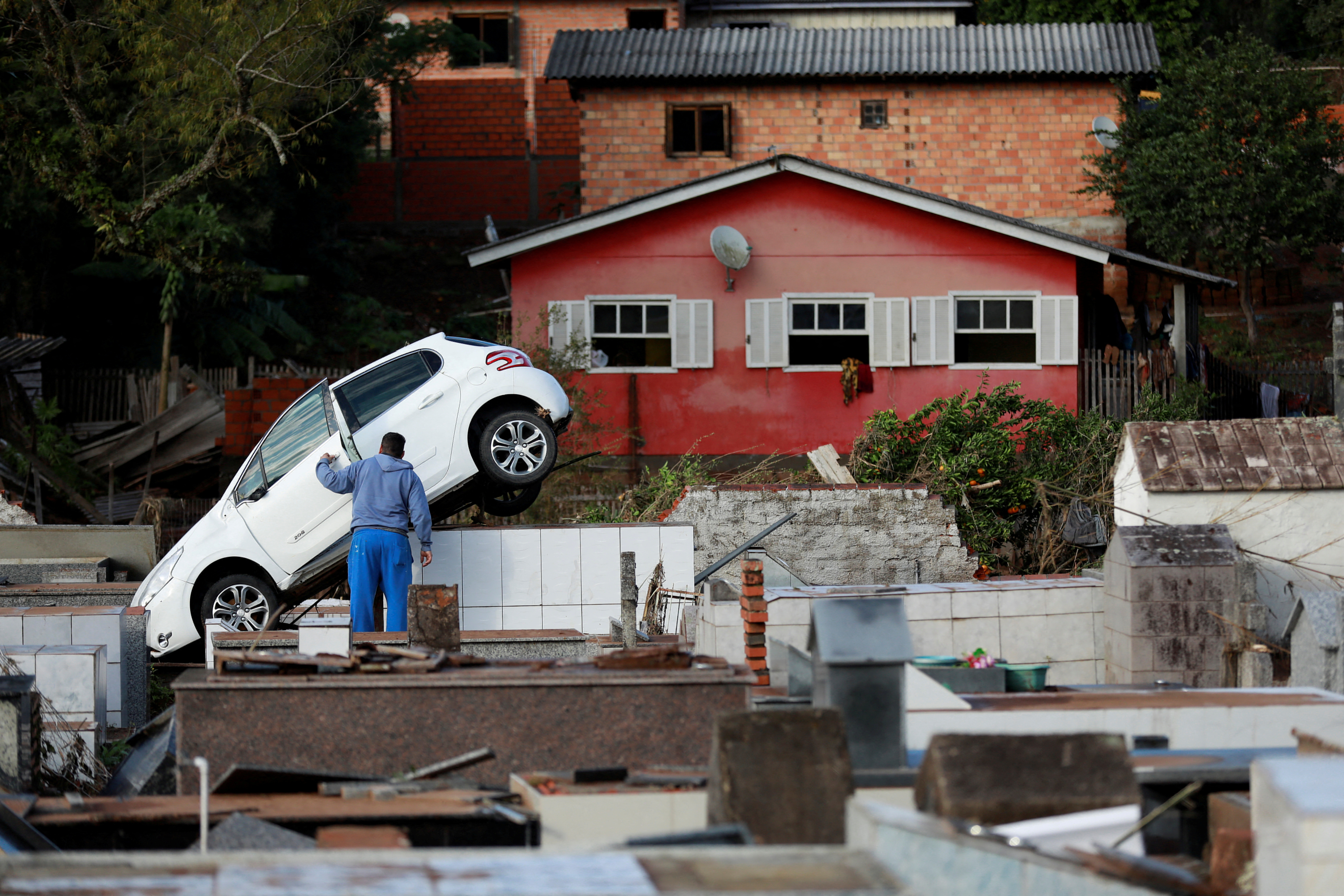 A man stands next to a car which came to rest on top of graves at the Pedro Freiberger cemetery as a result of flooding due to heavy rains following an extratropical cyclone, in Caraa