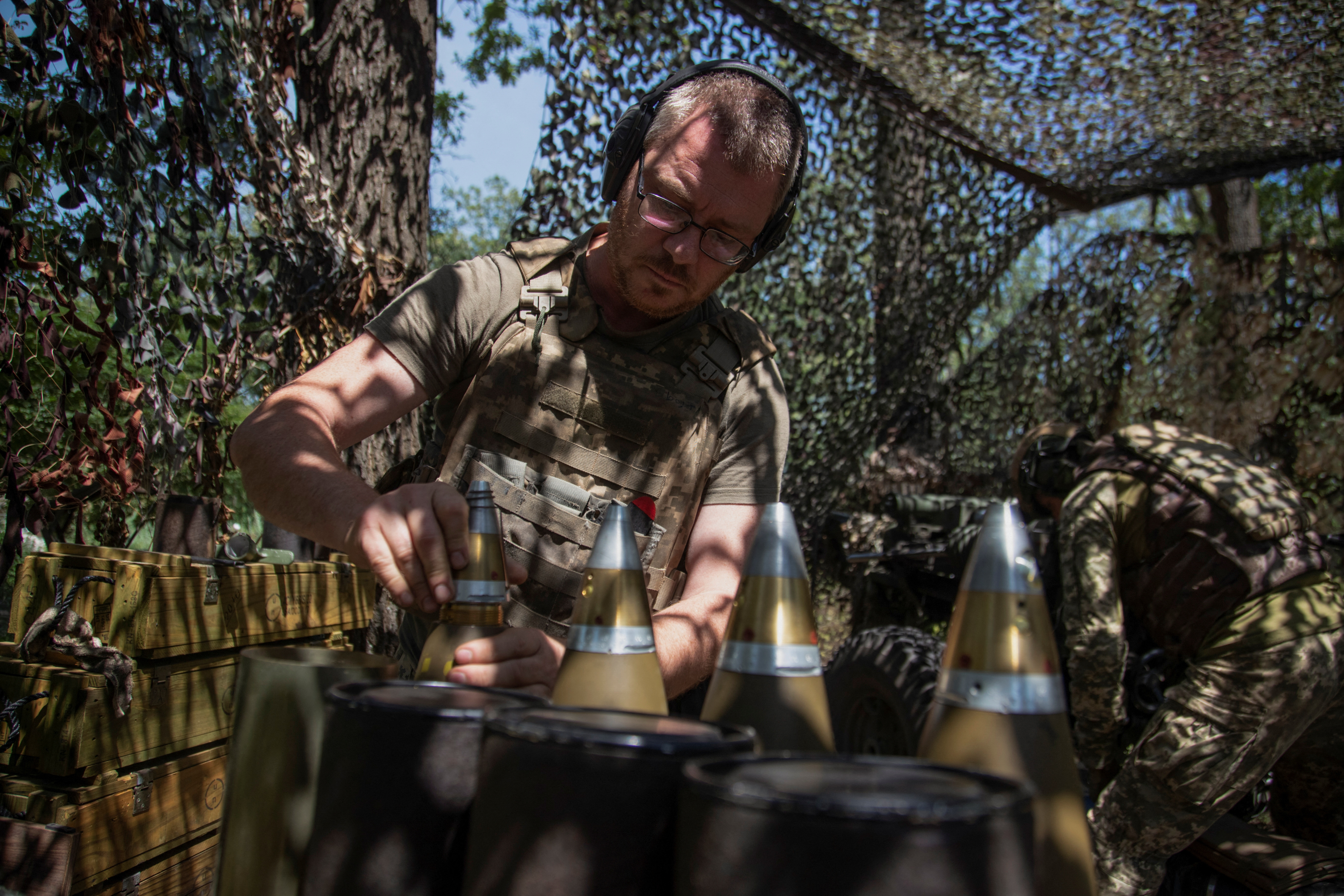 A Ukrainian soldier preparing shells for a howitzer. He is in a camouflaged position among trees