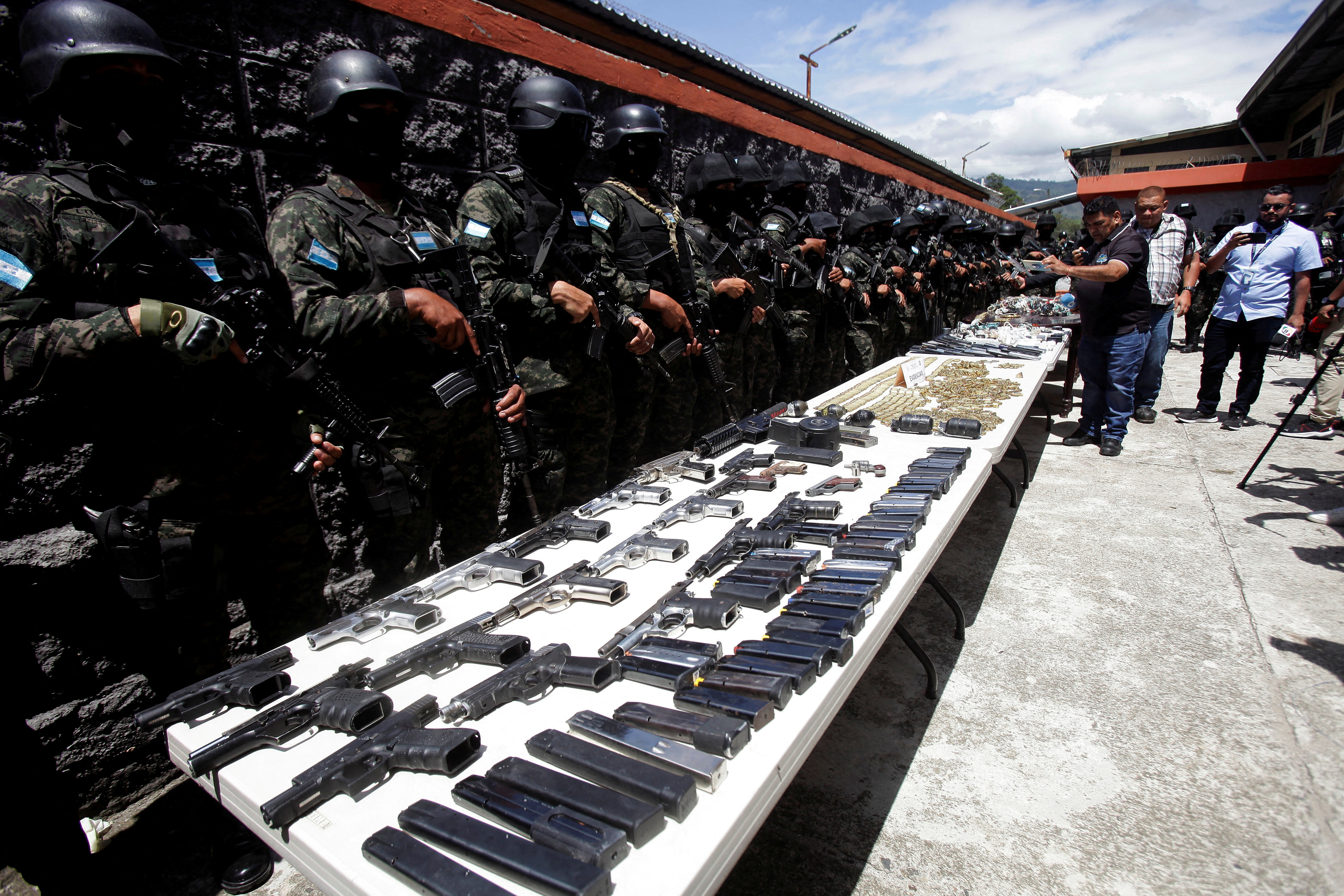 Guards stand behind a long white table, where guns and ammo are on display