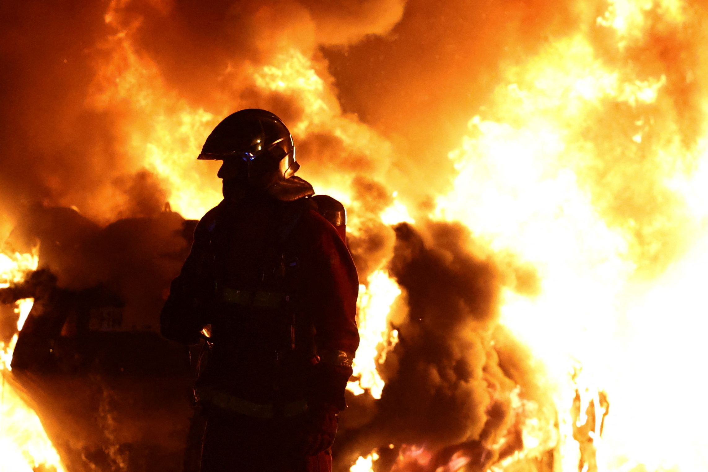 A firefighter stands in front of a burning vehicle during clashes between protesters and police, after the death of Nahel, a 17-year-old teenager killed by a French police officer during a traffic stop, in Nanterre, Paris suburb, France, June 28, 2023. REUTERS/Stephanie Lecocq
