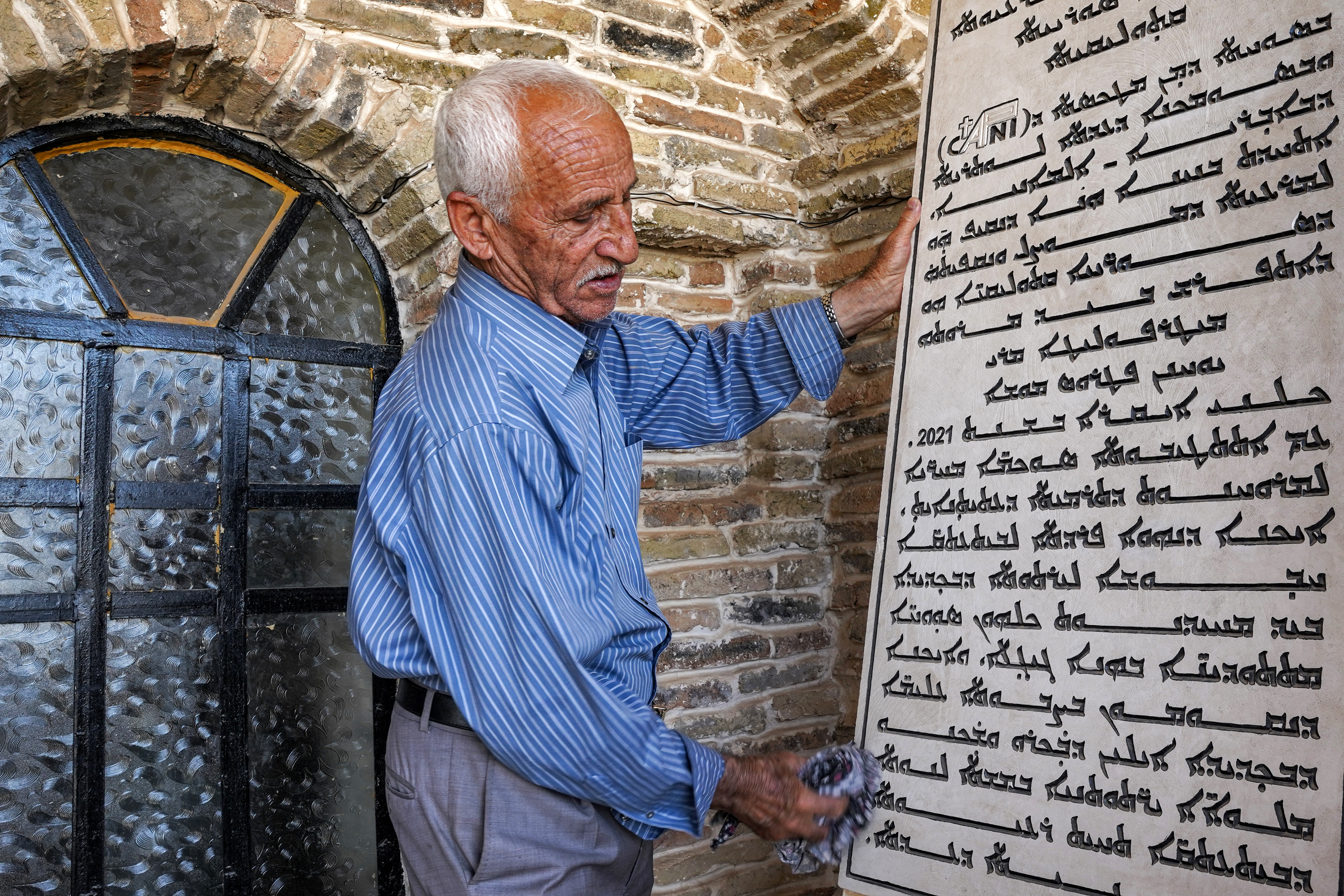 In this picture taken May 10, 2023 artist and museum curator Saliwa Shamoun Abba cleans a Syriac-inscribed plaque detailing information about the history of the Syriac Museum, in Iraq's predominantly Christian town of Qaraqosh