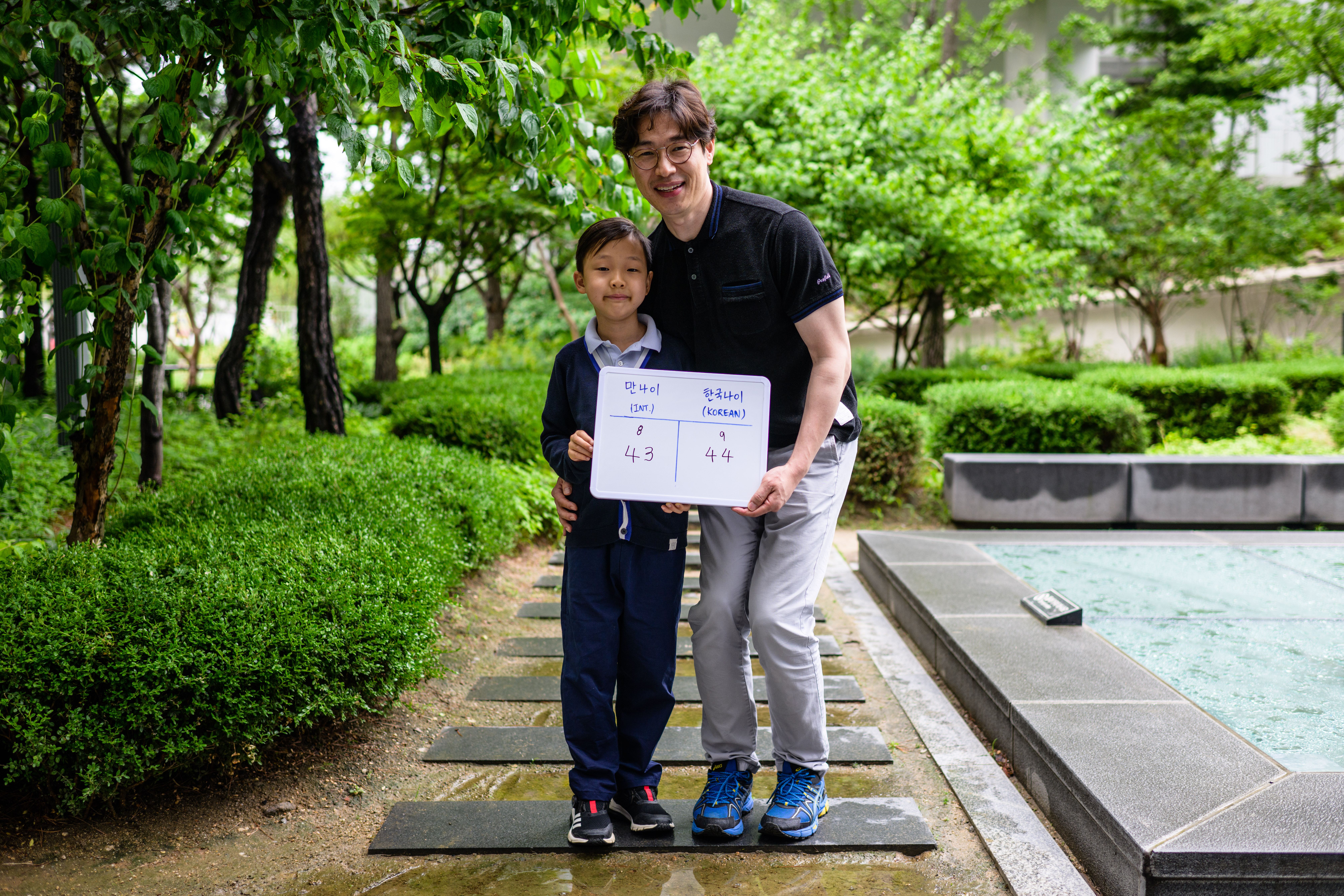 In this picture taken in Seoul on June 21, 2023, Yoon Jae-ha (L), poses with a whiteboard showing his international age, 8, and Korean age, 9, next to his father, Yoon Dong-gun, who works in trade, and whose international age is 43 and Korean age 44