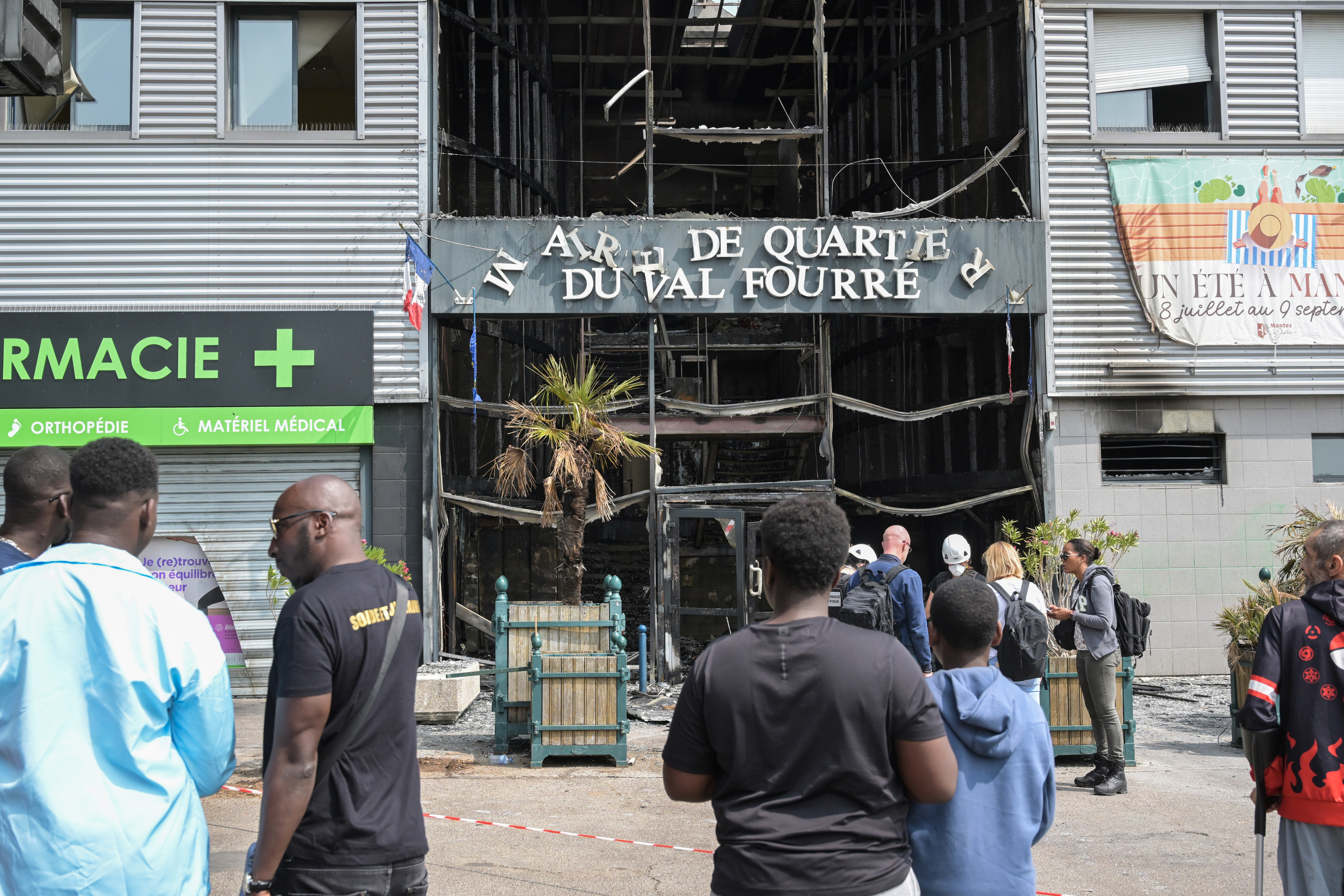 Local residents look on next to the facade of a burnt-down annex town hall of the Le Val Fouree neighbourhood in Mantes-la-Joli