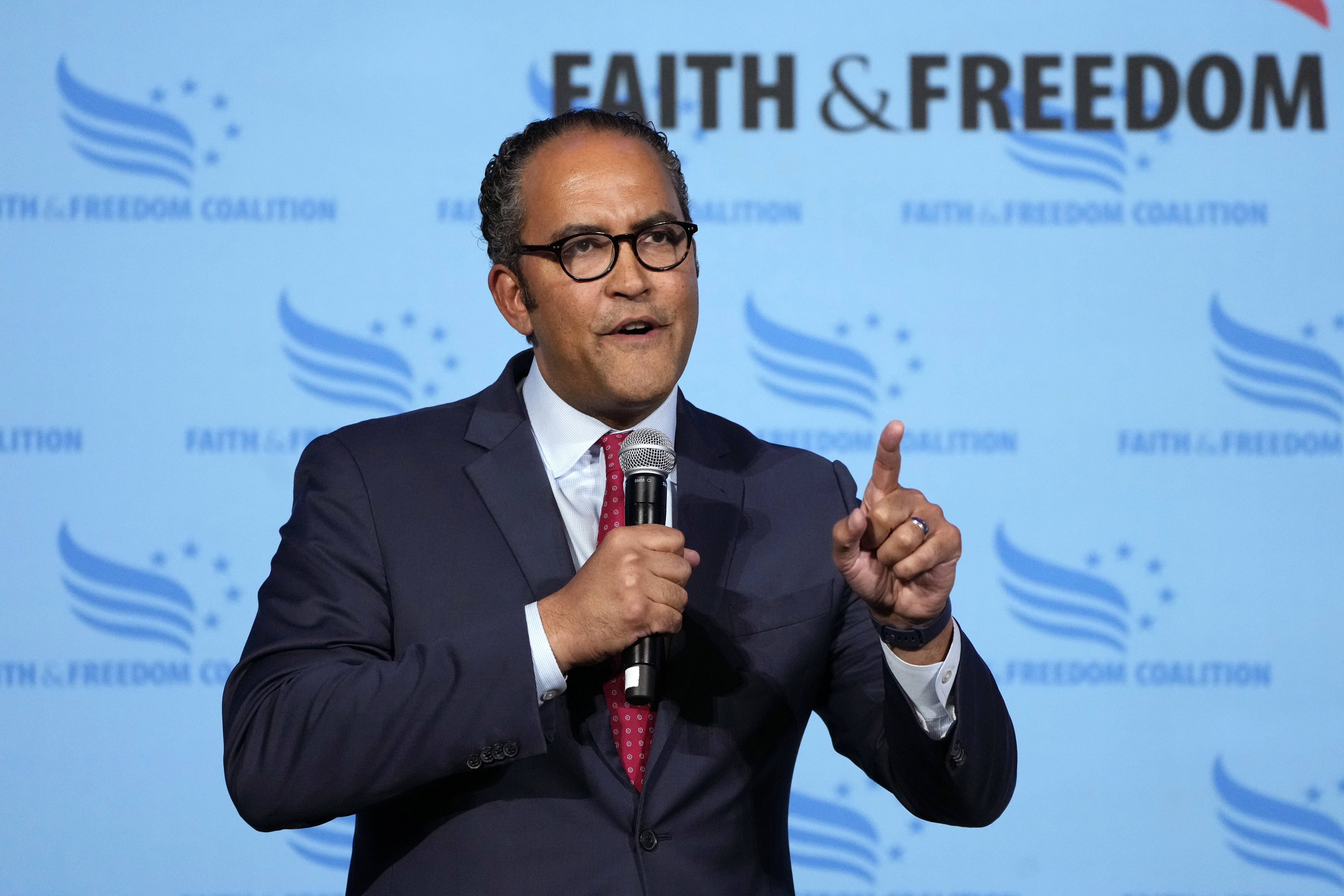 Will Hurd speaks into a microphone in front of a banner that reads "Faith & Freedom".