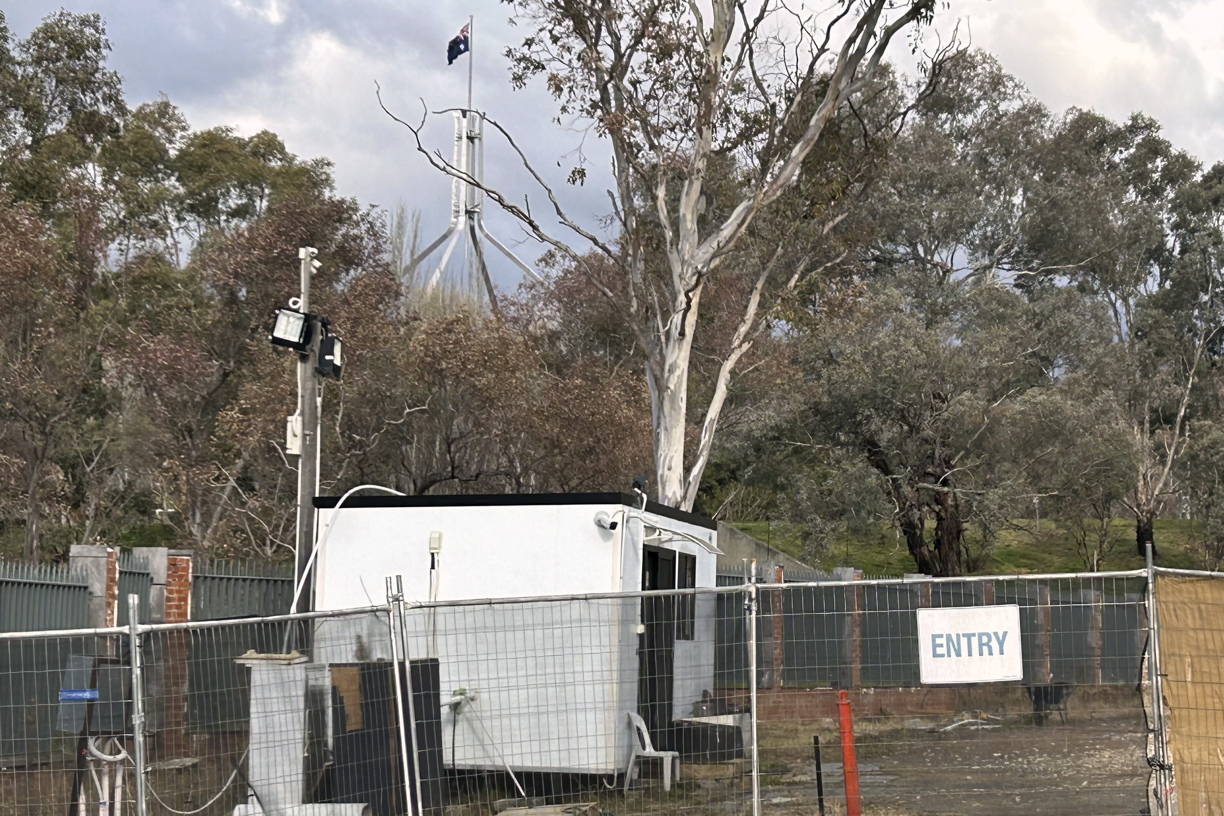 A flag files above Australian house. In front is the site of the land Russia leased to build its new embassy. There's a cabin on the site, fencing and trees.