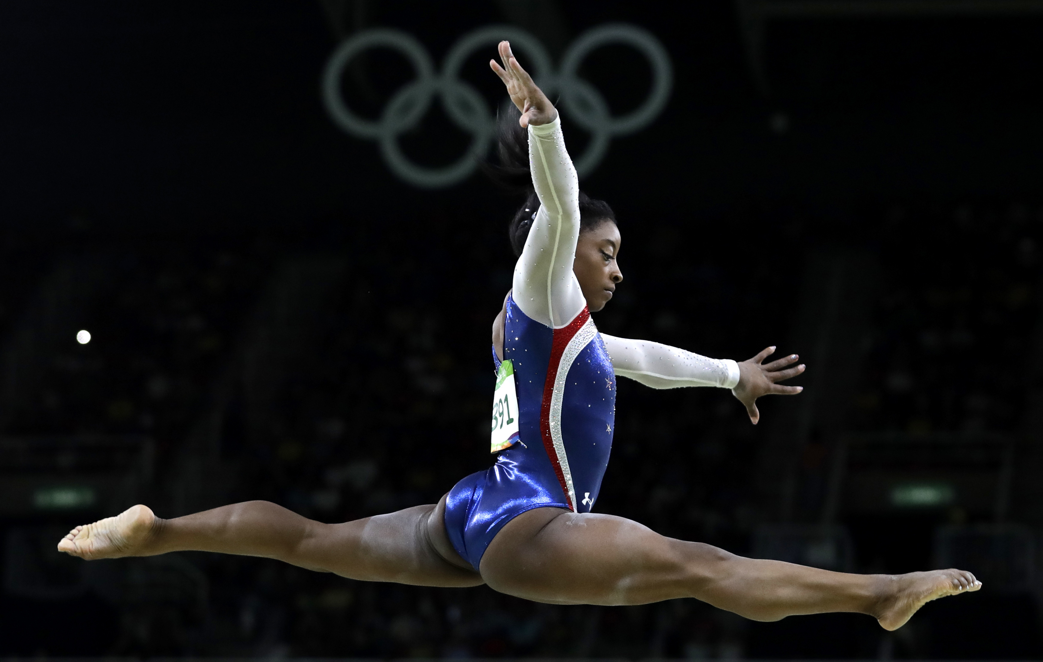 A woman gymnast does a split flying through mid-air.