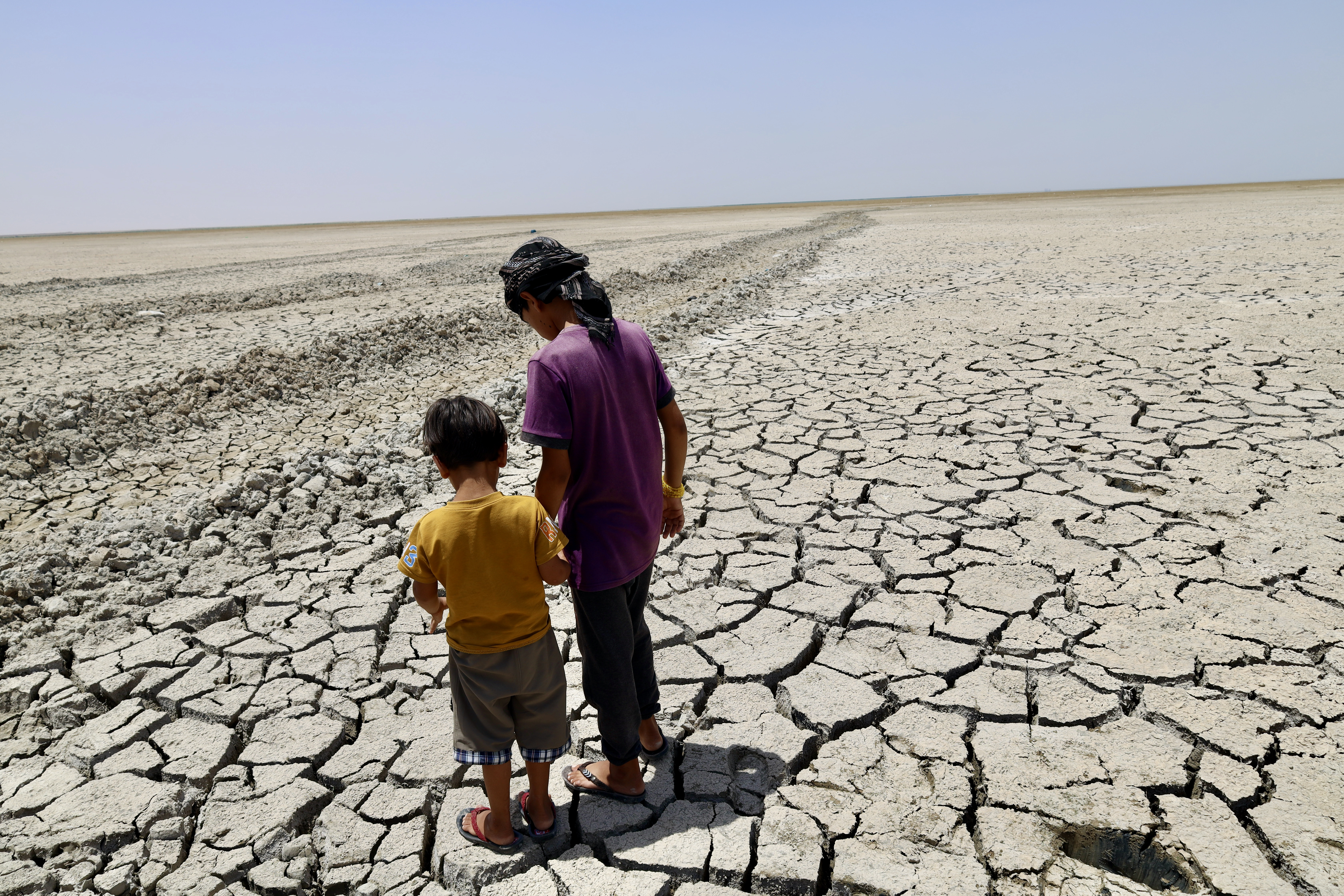 Two young boys from the village, 13-year-old Rusool and 6-year-old Waad, explore the cracked ground where the water used to sit.